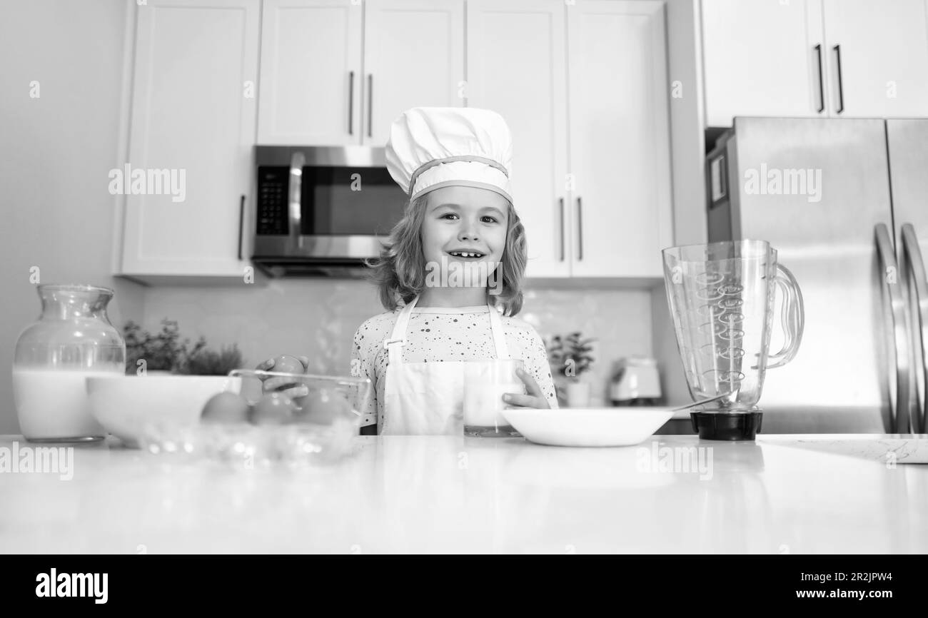 Cuoco del capretto cuoco nel cappello del cuoco che prepara il cibo sulla cucina. Bambino che rende gustoso delizioso. Cucina pasto. Foto Stock