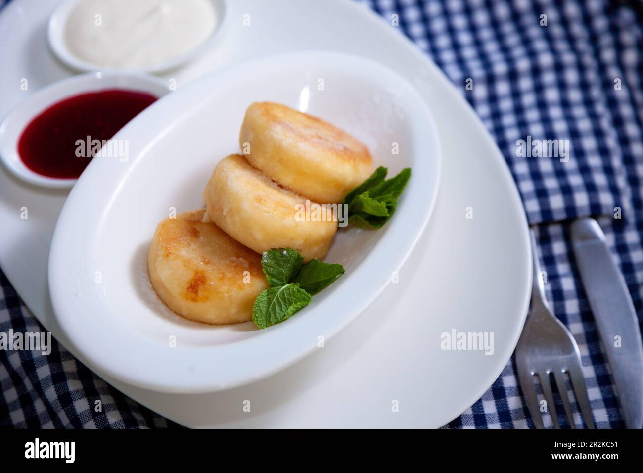 Frittelle di formaggio ricotta rotonda in un piatto bianco su sfondo blu. Cibo prima colazione. Cibo sano. Salsa di panna acida e menta. Primo piano vista dall'alto. Pasto dessert. Frittelle di ricotta al formaggio ricotta. Foto Stock