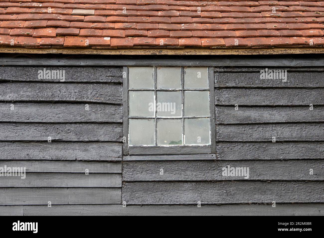 Legno nero, tetto piastrellato, fienile Sussex con finestra quadrata con nove pannelli finestra quadrata primo piano dettaglio che forma il disegno astratto Foto Stock