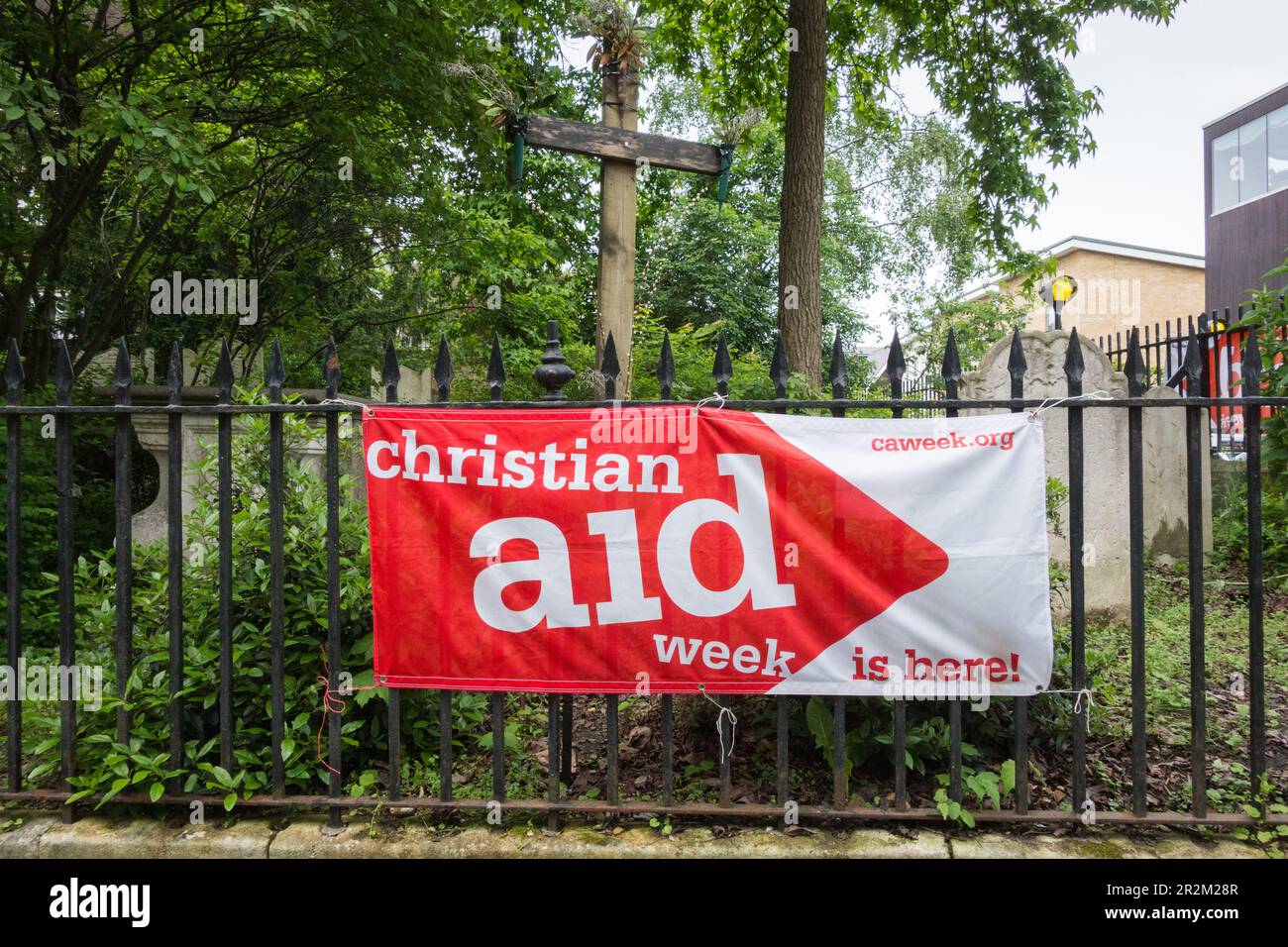 Christian Aid Week è qui banner al di fuori della chiesa di St Mary the Virgin, Mortlake High Street, Mortlake, Londra, SW14, Inghilterra, Regno Unito Foto Stock