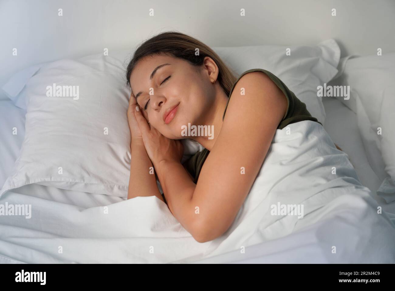 Giovane donna che dorme profondamente nelle lenzuola bianche di notte Foto Stock