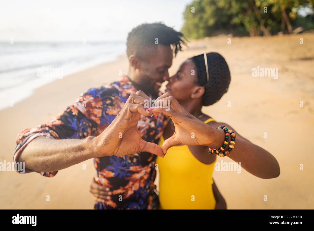 Due amanti sulla spiaggia fanno i cuori con le mani e hanno un momento appassionato Foto Stock