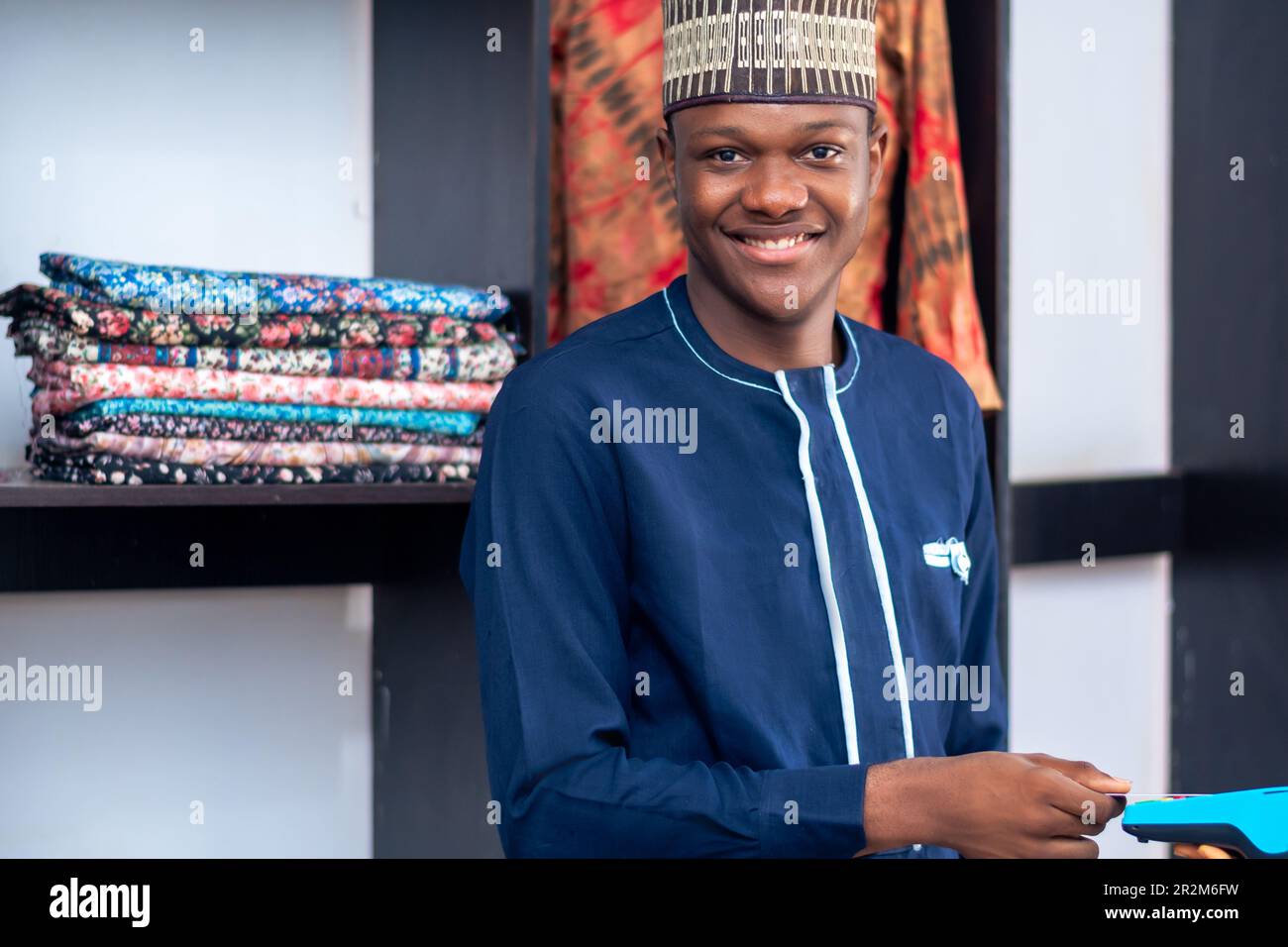 uomo africano che vende in un mercato della moda utilizzando una macchina punto vendita e sorridendo. Metodo di pagamento, transazione senza contanti Foto Stock