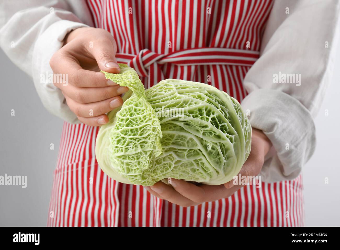 Donna che separa foglia da verza fresca su fondo grigio chiaro, primo piano Foto Stock