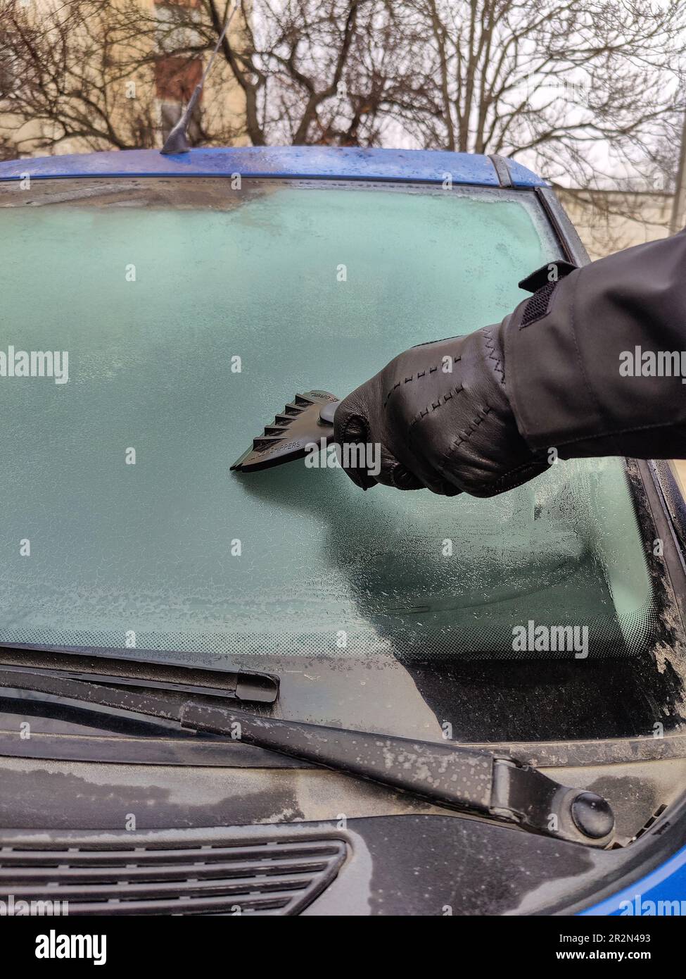 L'uomo raschia il gelo con un raschietto di plastica dal finestrino  laterale di un'automobile