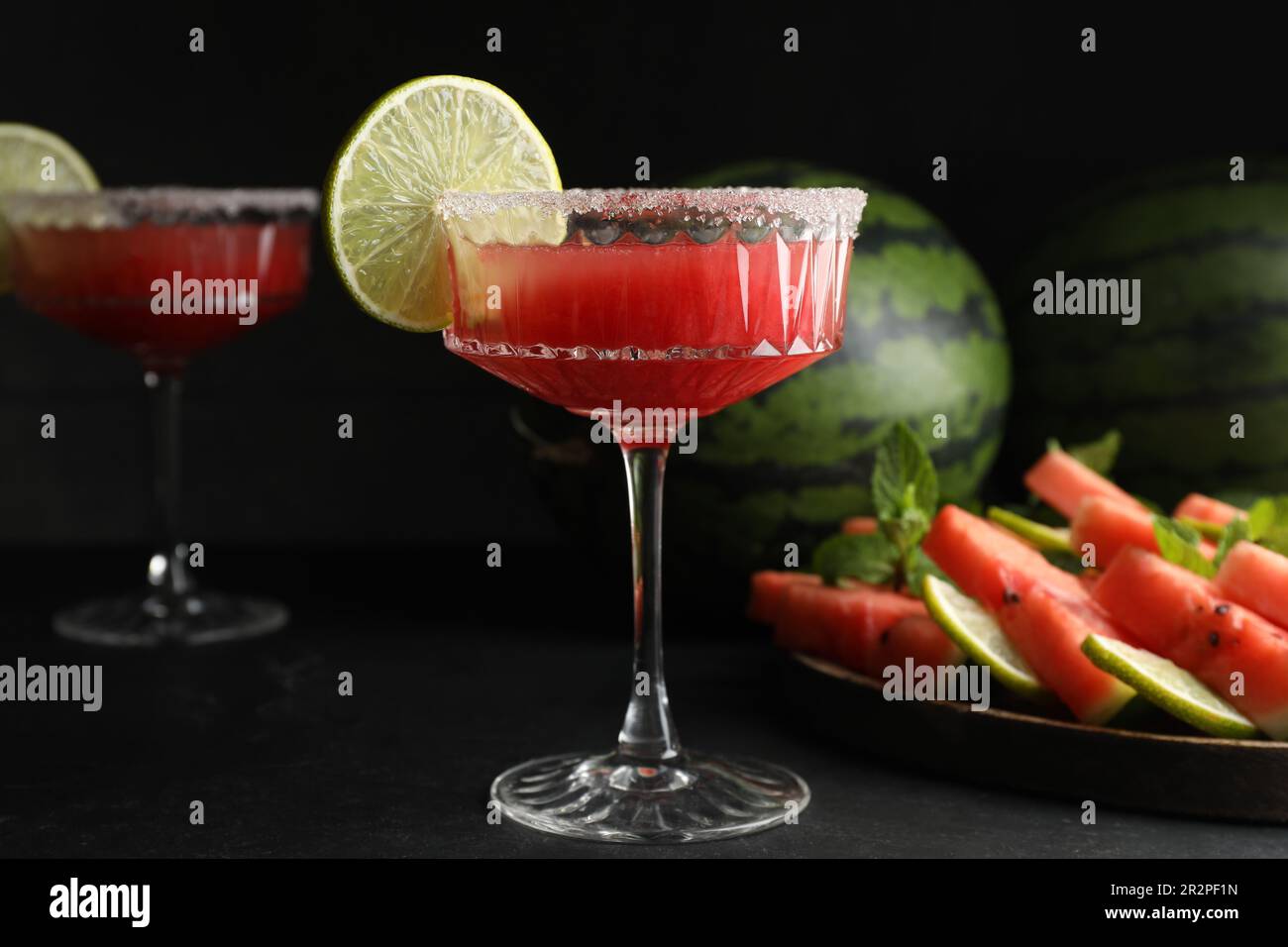 Bicchieri da cocktail di delizioso succo di cocomero fresco con lime e zucchero sul tavolo nero Foto Stock