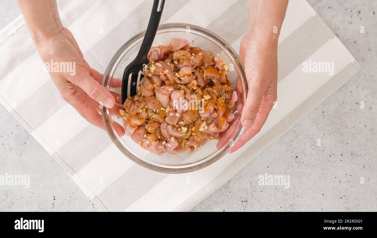 Ciotola di vetro con la miscela di carne di pollo marinata tritata all'interno, piatto, spazio copia, mani di donna Foto Stock