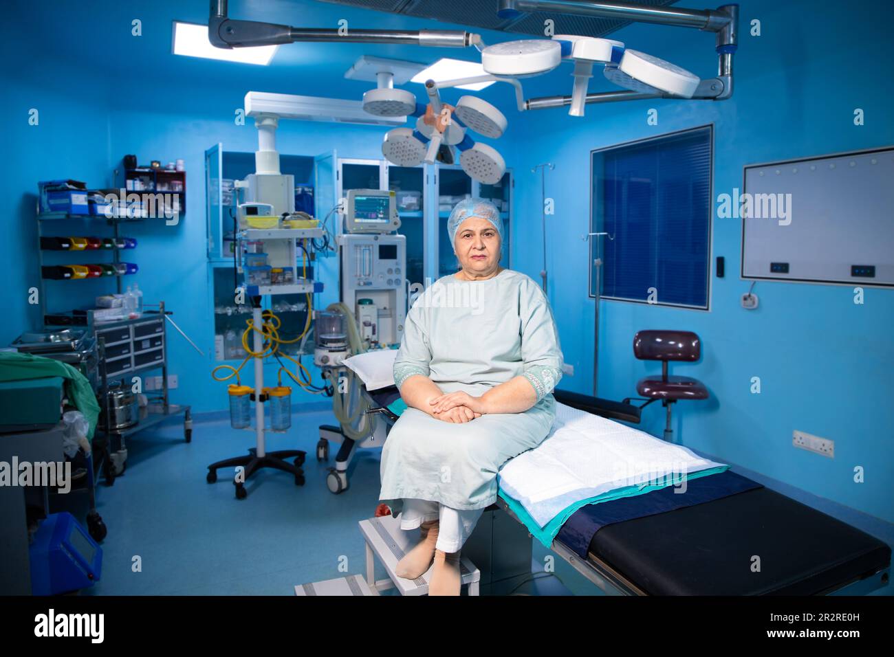 Ritratto di un paziente indiano anziano seduto in teatro operatorio pronto per l'intervento chirurgico in ospedale. Concetto sanitario e medico. Lunghezza intera Foto Stock
