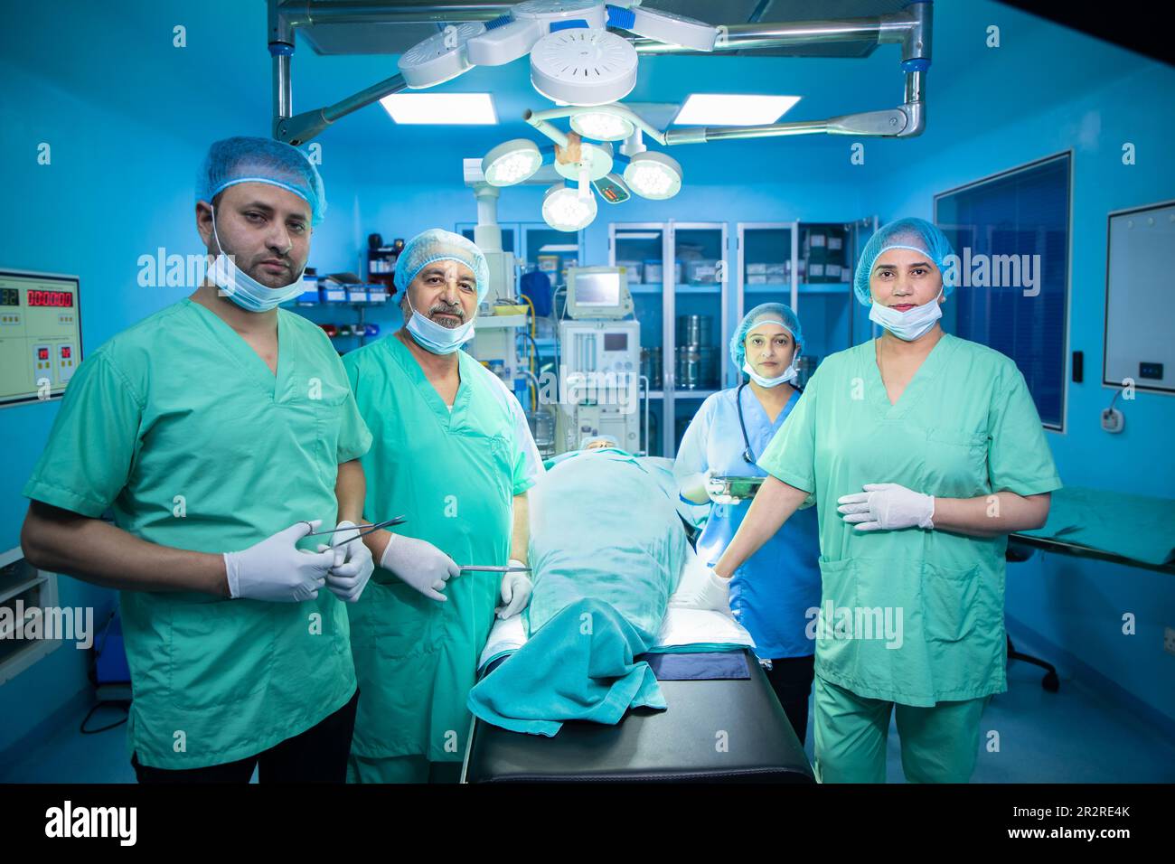 Team di chirurghi indiani personale medico indossando maschera e cappuccio guardando la fotocamera dopo aver eseguito con successo l'intervento chirurgico in teatro operatorio in ospedale Foto Stock