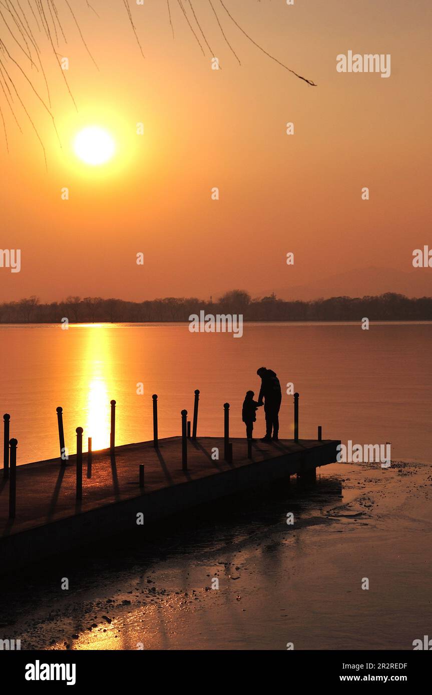 Silhouette di famiglia felice sullo sfondo di mare, sole, nuvole sfondo su arancione tramonto in mare Foto Stock