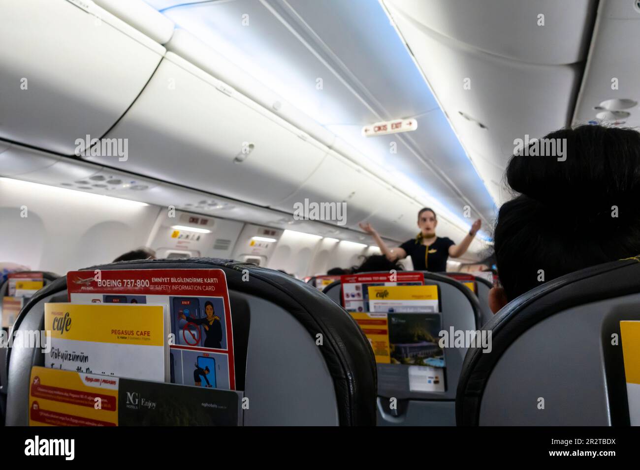 Assistente di volo donna fuori fuoco che mostra uscite di emergenza ai passeggeri seduti su sedie di un Boeing 737-800, Pegasus, compagnia aerea turca Foto Stock