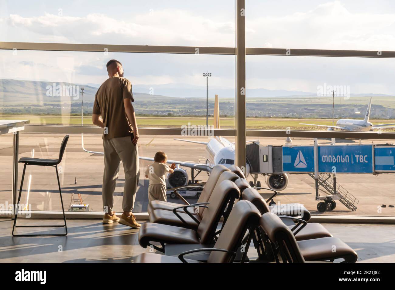 Area d'attesa dell'Aeroporto Internazionale di Tbilisi, padre e bambino che guardano il campo aereo attraverso la finestra TBS, Tbilisi, Georgia Foto Stock