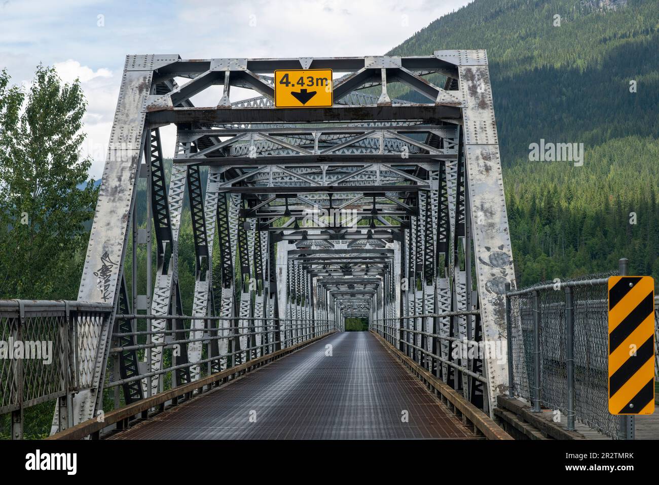 La prospettiva dei conducenti di un ponte a capriate in acciaio attraverso il fiume nella zona montagnosa del Canada con ponte di griglia in acciaio e segni che indicano maxi Foto Stock