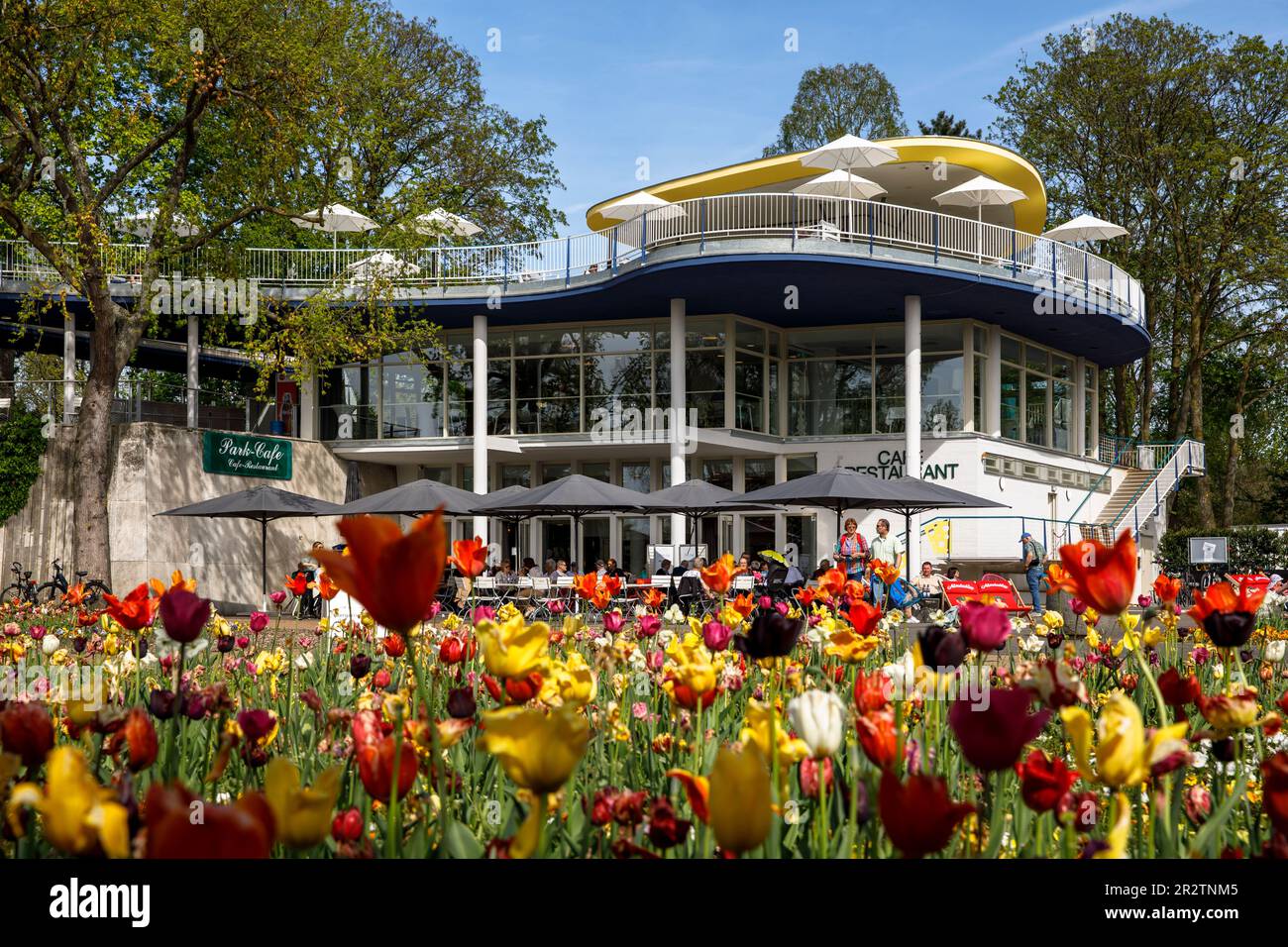 Lo storico Park Café nel Parco del Reno nel quartiere Deutz, zona ricreativa locale, letti con tulipani, Colonia, Germania. Das historische Park-Café Foto Stock