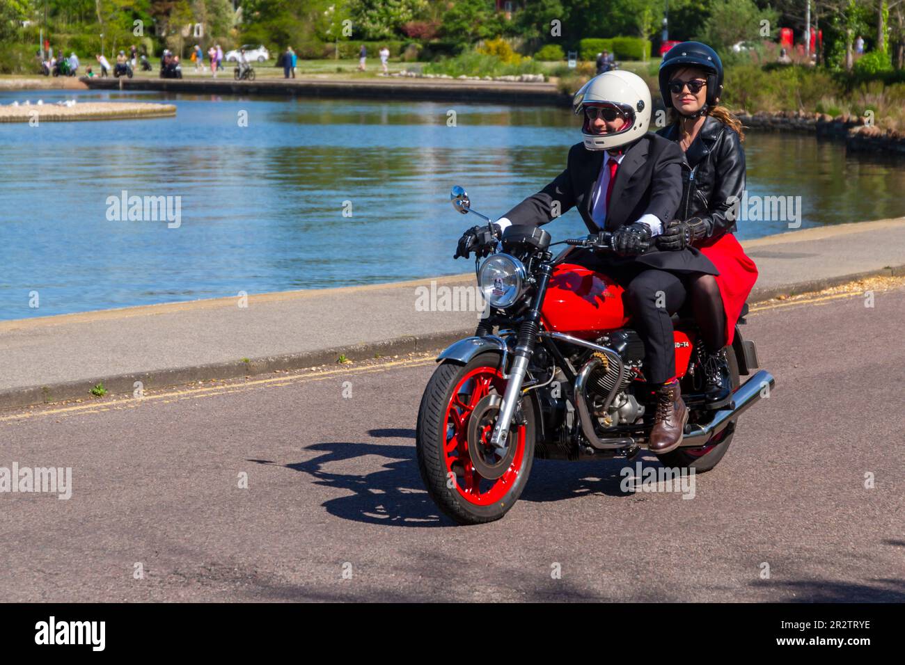 Poole, Dorset, Regno Unito. 21 maggio 2023 Bournemouth and Poole Distinguished Gentlemen's Ride è un evento annuale, uno dei tanti in tutto il mondo, per raccogliere fondi e sensibilizzare sulla salute degli uomini. Durante il loro viaggio, centinaia di moto, molte vintage, attraversano Poole Park sulla strada per Bournemouth con molti dei loro piloti vestiti in modo appropriato, in stile retrò cravatte, baffi e tweeds in una bella giornata di sole. Uomo vestito con giacca e cravatta sorridente con passeggero femminile in sella alla moto moto rossa Moto Guzzi T4 Credit: Carolyn Jenkins/Alamy Live News Foto Stock