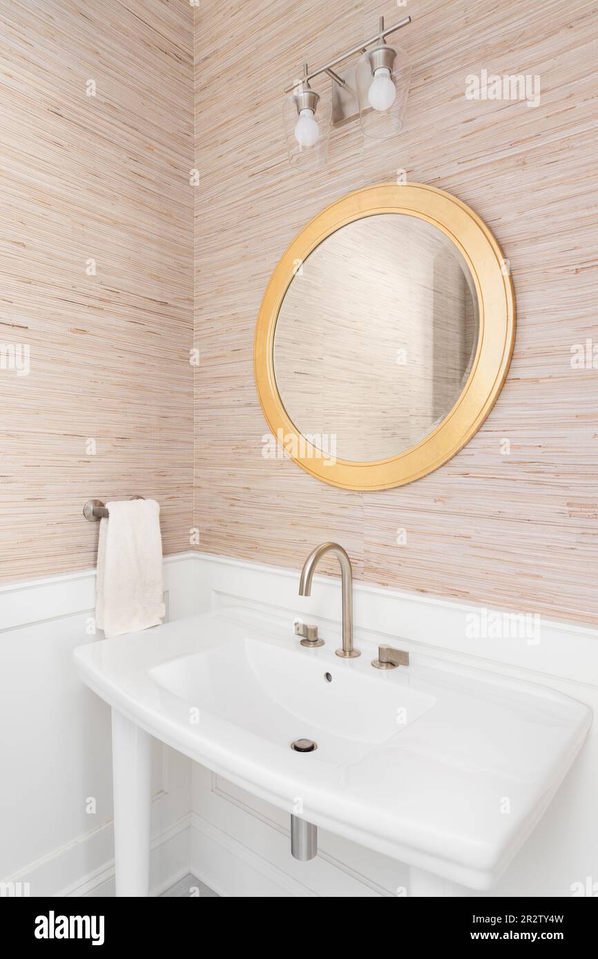 Un bagno con carta da parati marrone, un lavandino a piedistallo bianco,  specchio circolare dorato, lavagna bianca e pareti a listelli Foto stock -  Alamy