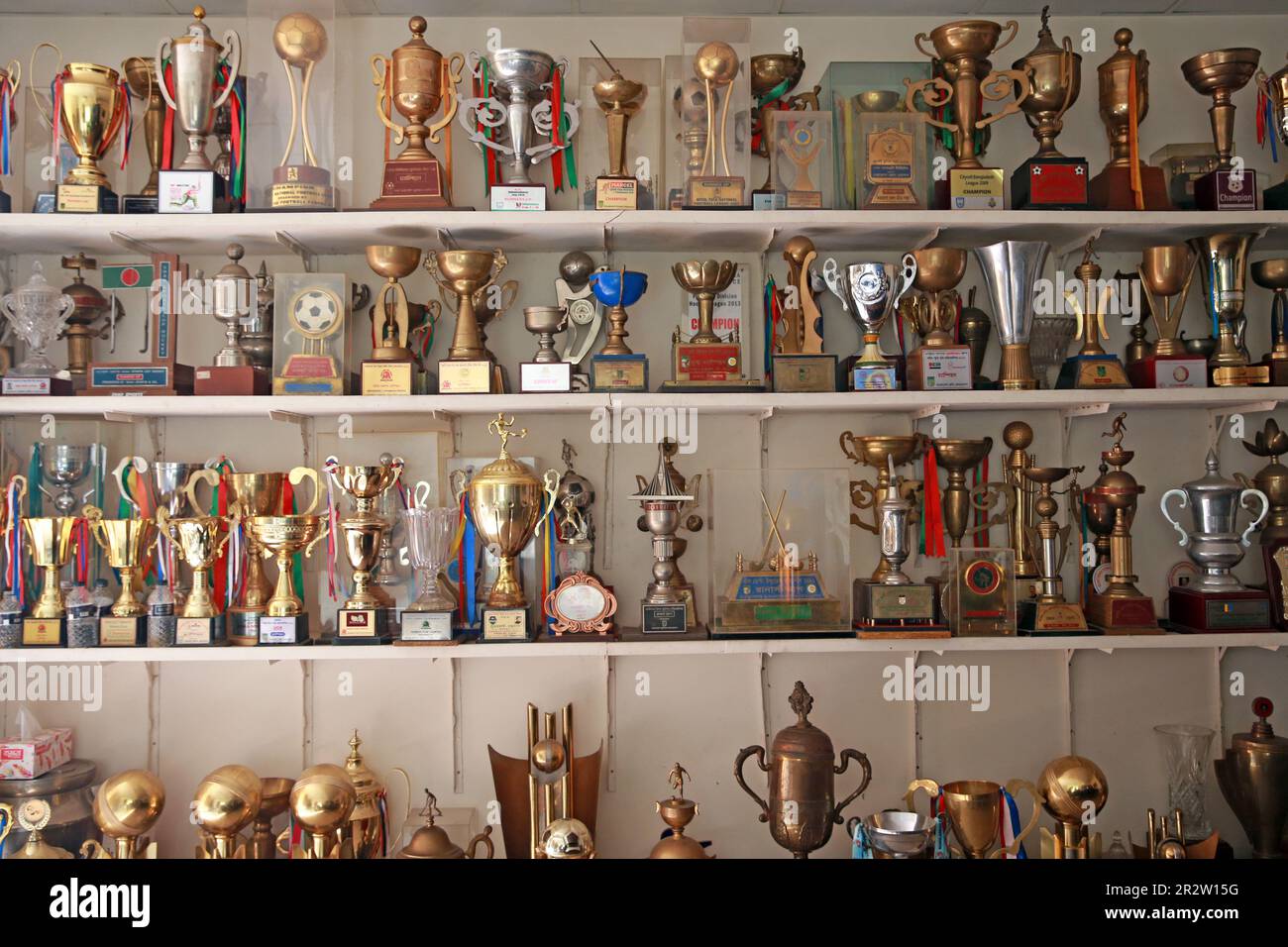 I trofei per i tornei vincenti in vari momenti vengono visualizzati nella sala del consiglio di amministrazione di Abahani Ltd. Club come calciatori partecipano alla sessione di parctice al club groun Foto Stock