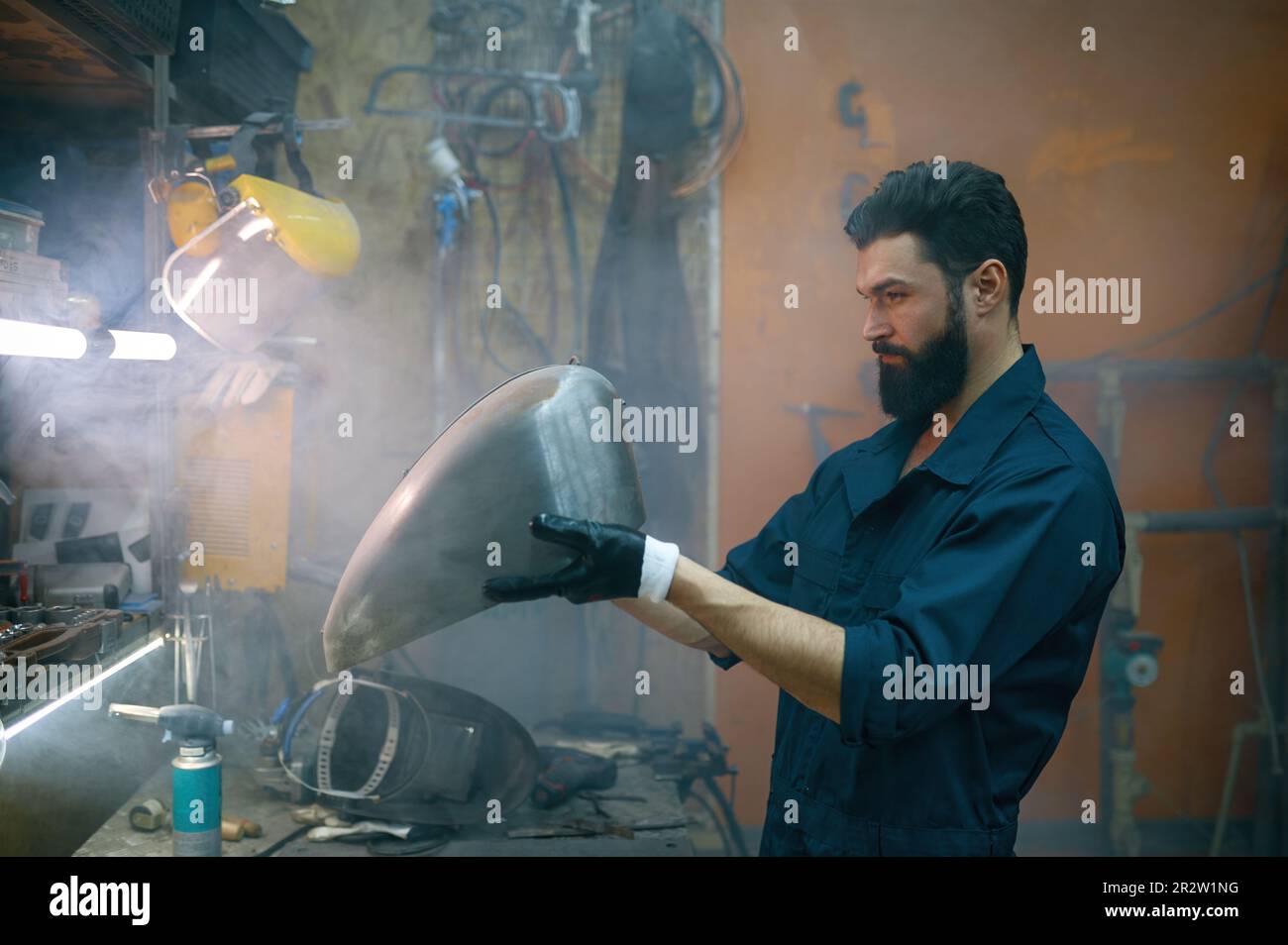 Riparatore concentrato serio che ispeziona la nuova parte saldata per motociclo Foto Stock