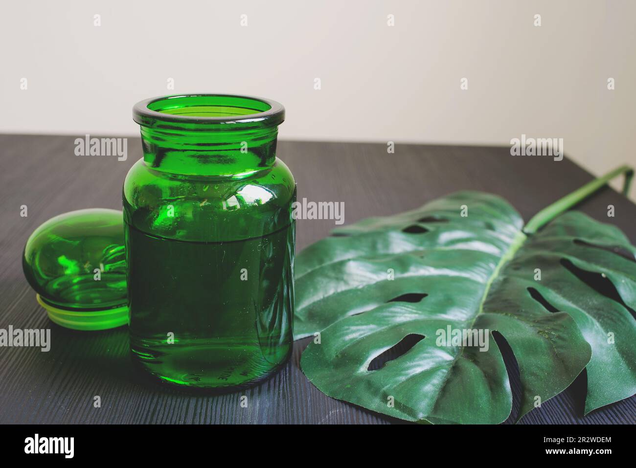 Bottiglia verde sul tavolo con Monstera su fondo nero. Concetto e minimalismo. Foto Stock