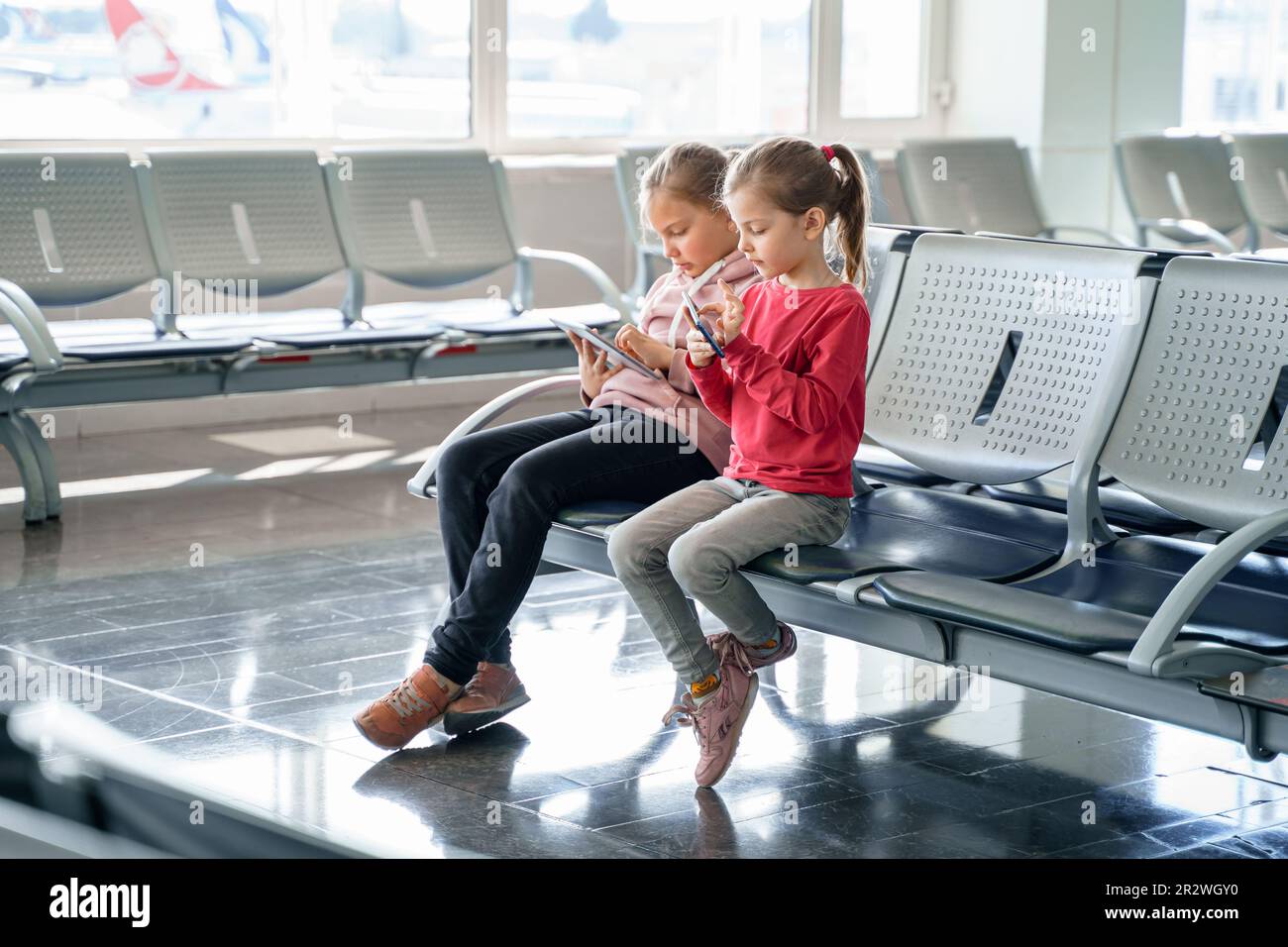 Bambini, bambini, ragazze in attesa di volo in aereo nella sala partenze. Sedersi sulle sedie, giocare a giochi per computer in gadget, telefono cellulare, tablet. Chat in corso Foto Stock