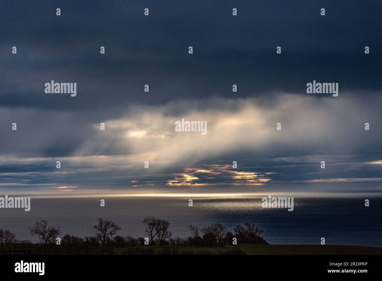 Raggi di luce che brillano attraverso le nuvole scure sulla costa di Angus, Scozia Foto Stock