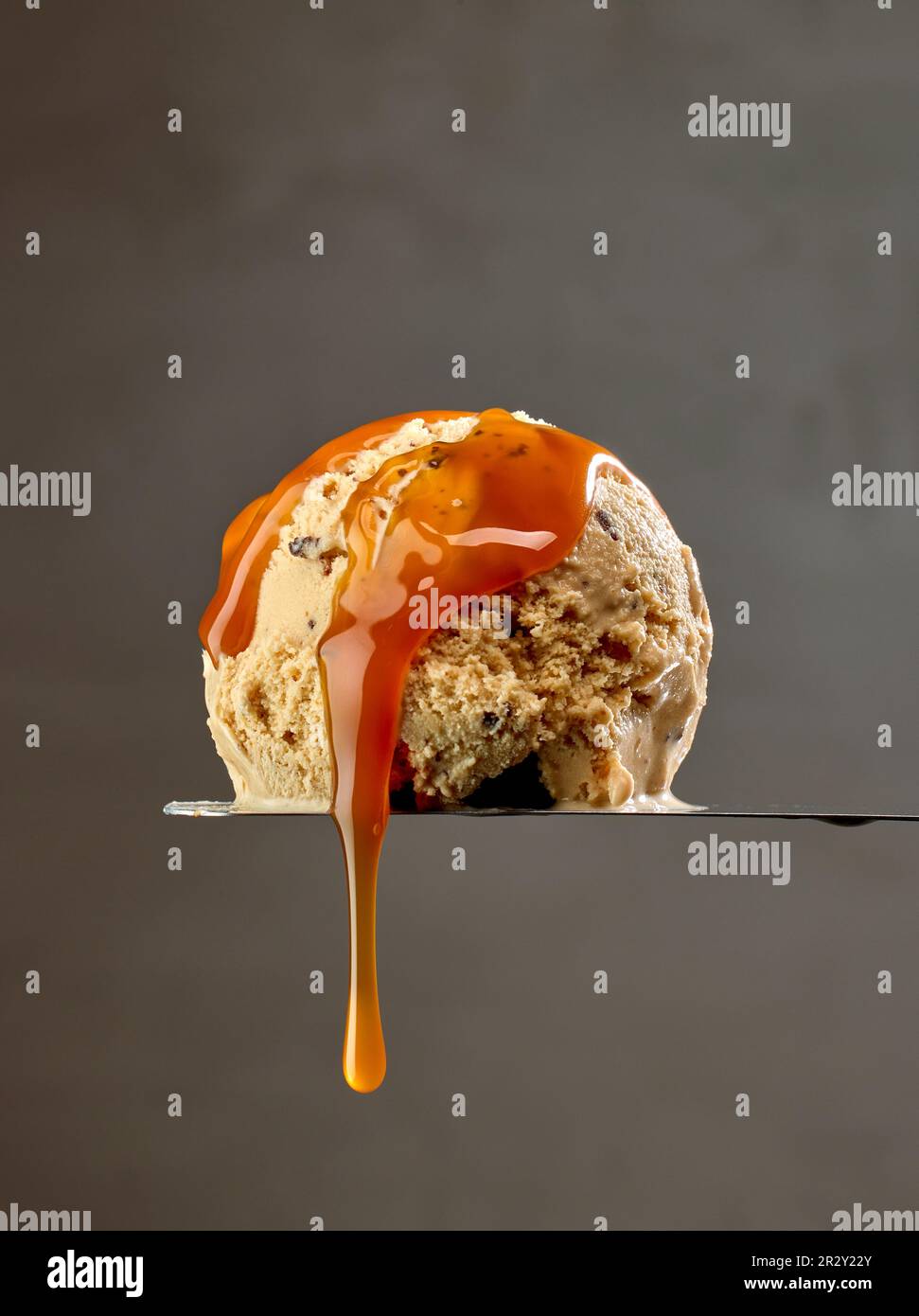 paletta per gelato con salsa al caramello sciolta scorrevole su fondo parete grigio scuro Foto Stock