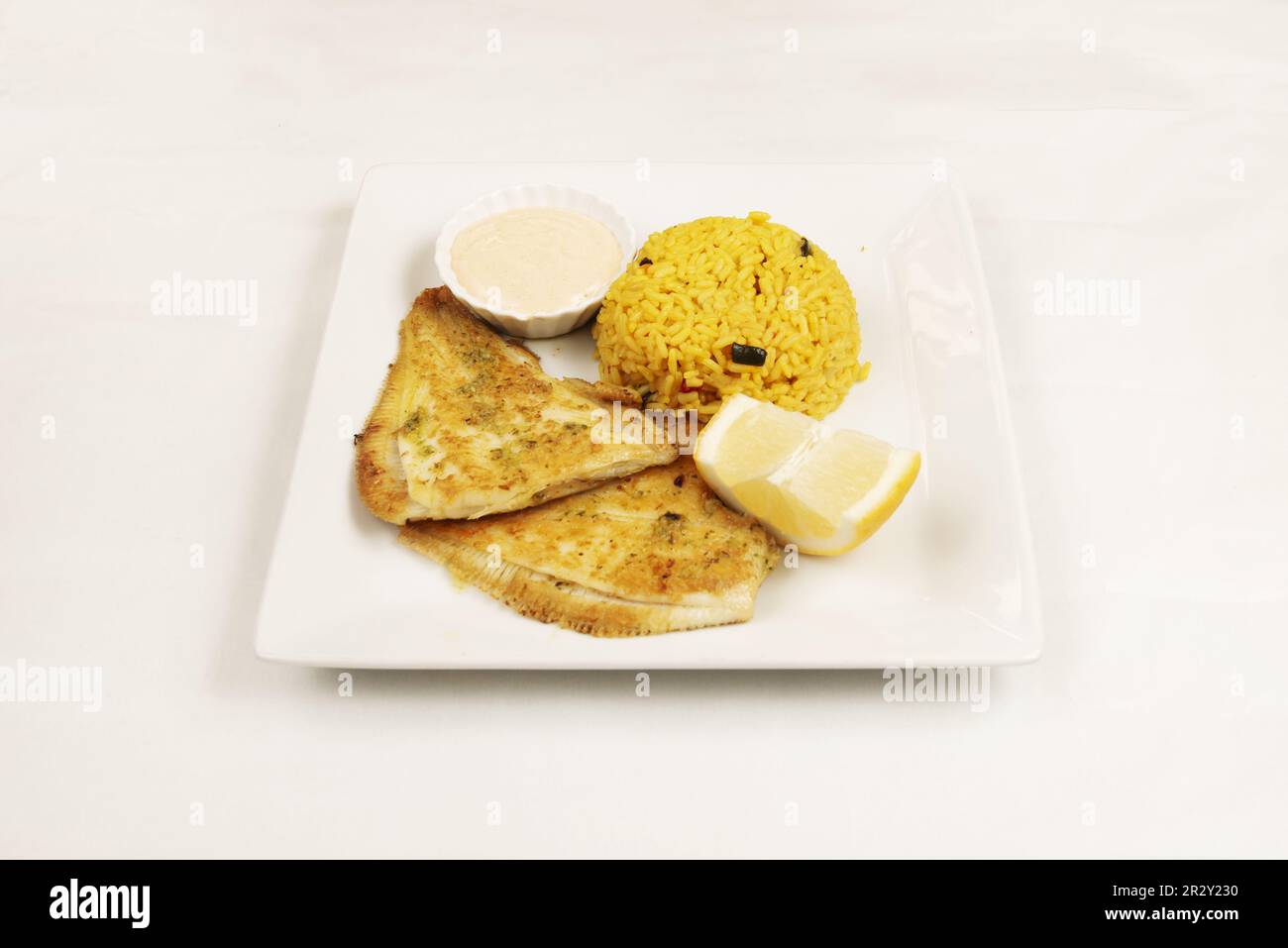 Un piatto quadrato bianco con una ricetta per il gallo fritto con una ciotola di riso, salsa e limone Foto Stock