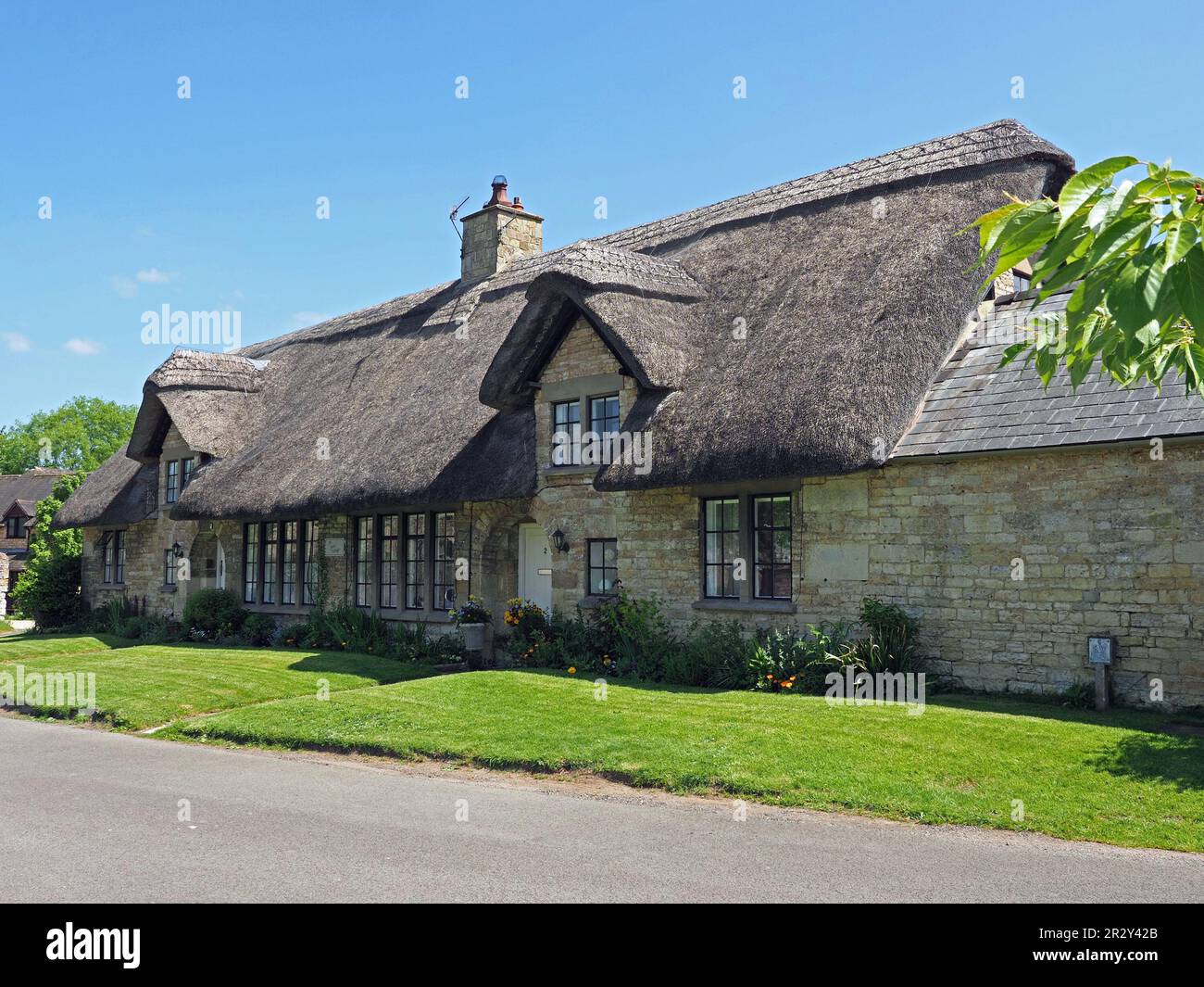 Cartolina Cotswold cottage in paglia con pietra di miele sotto il cielo blu con prato ordinato in Gloucestershire, Inghilterra, Regno Unito Foto Stock