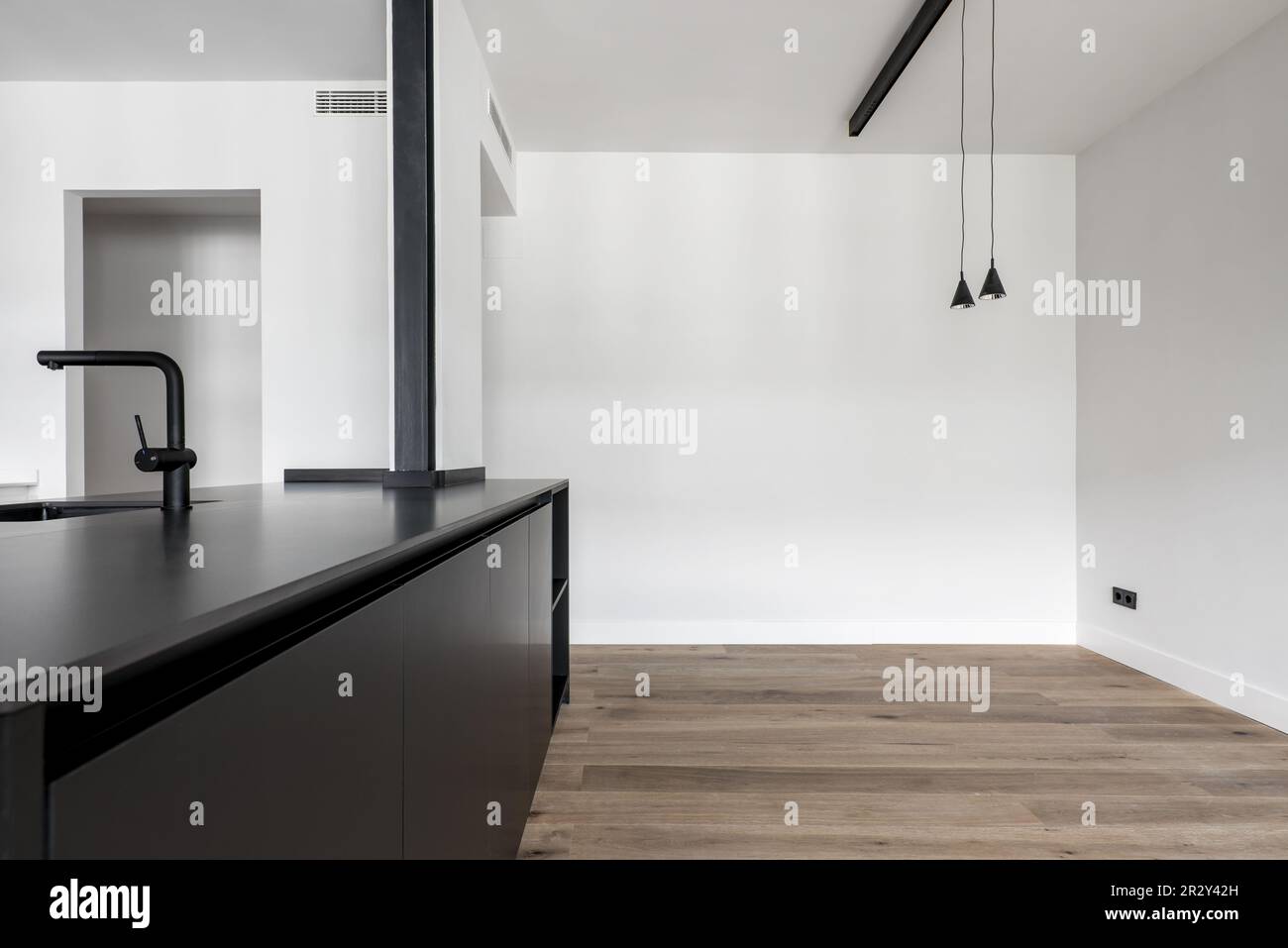 Soggiorno con pareti bianche e cucina dotata di portello di servizio e lavandino con rubinetto nero, pavimenti in legno di quercia e lampade da soffitto nere appese ad un Foto Stock
