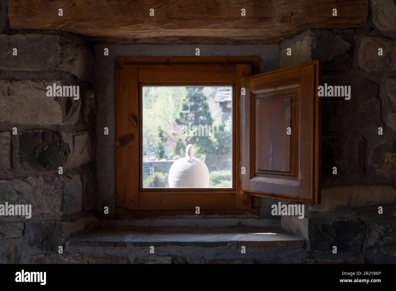 un botijo bianco visto dall'interno di una finestra di una casa di villaggio in pietra con persiane in legno, tipico botijo in argilla spagnola per mantenere l'acqua fresca in s Foto Stock