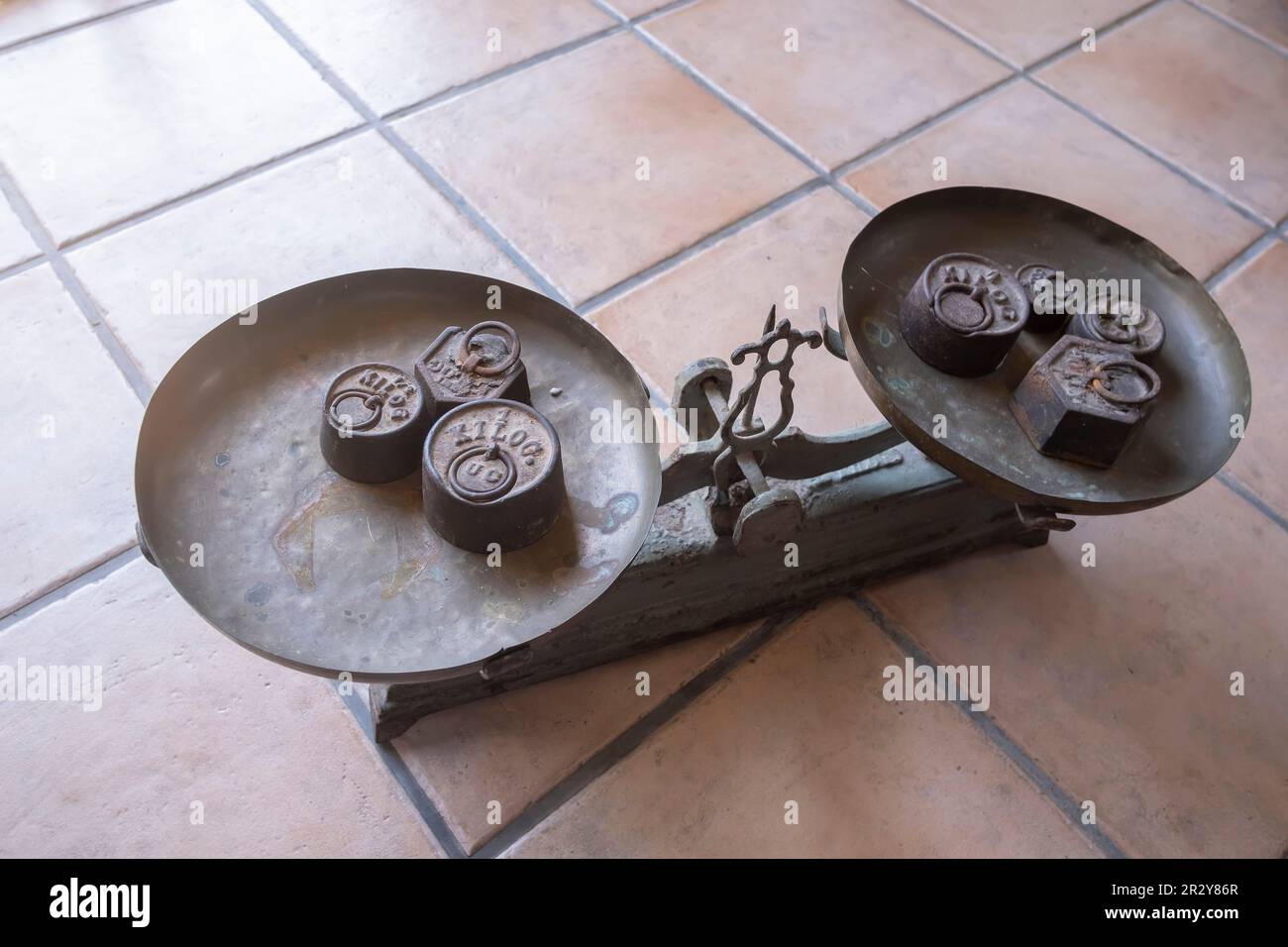 una scala antica con pesi di diverse dimensioni su entrambi i lati, su un pavimento rustico, vecchio peso, antico equilibrio d'annata, vecchie scale su una superficie piastrellata, s Foto Stock