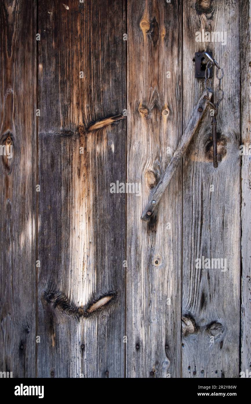 una vecchia porta in legno, intemperita dal passare del tempo con una chiave antica inserita nella serratura, usurata tessitura in legno, verticale Foto Stock