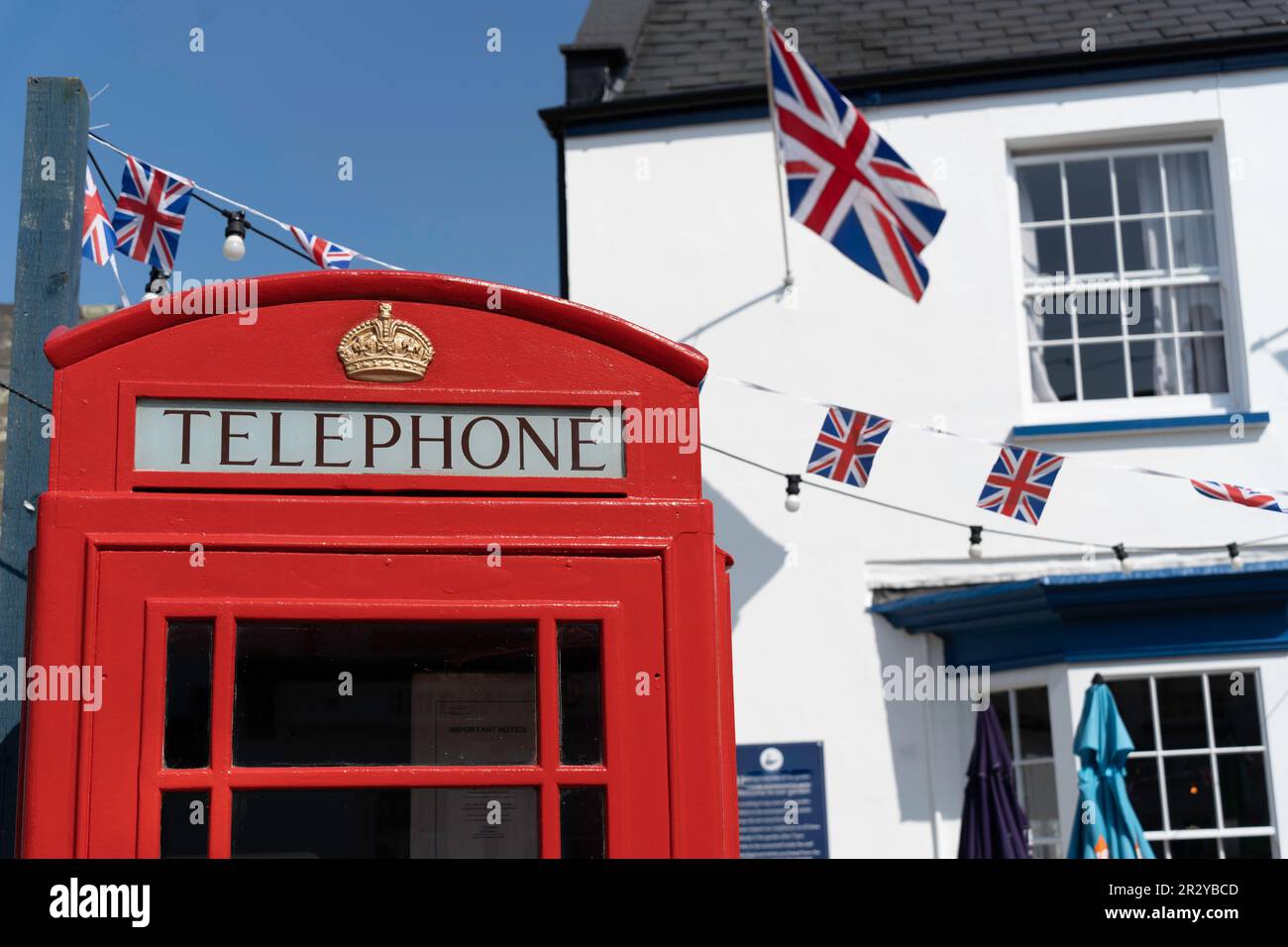 Scatola telefonica rossa britannica con un tipico pub britannico sullo sfondo e bandiere Union Jack, bunting Foto Stock