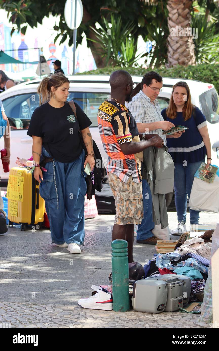 Un uomo acquista un articolo di abbigliamento da un uomo africano in un mercato di strada all'aperto regolamentato dalla polizia a Lisbona, Portogallo, aprile 2023. Foto Stock