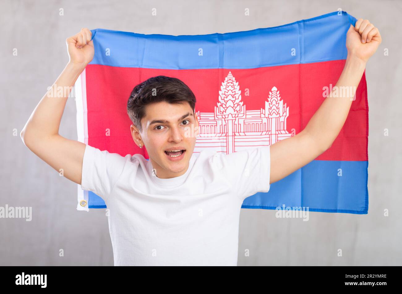 Eccitato, attivo spettatore maschile tiene bandiera nazionale della Cambogia in mani e canti slogan popolare. Foto Stock