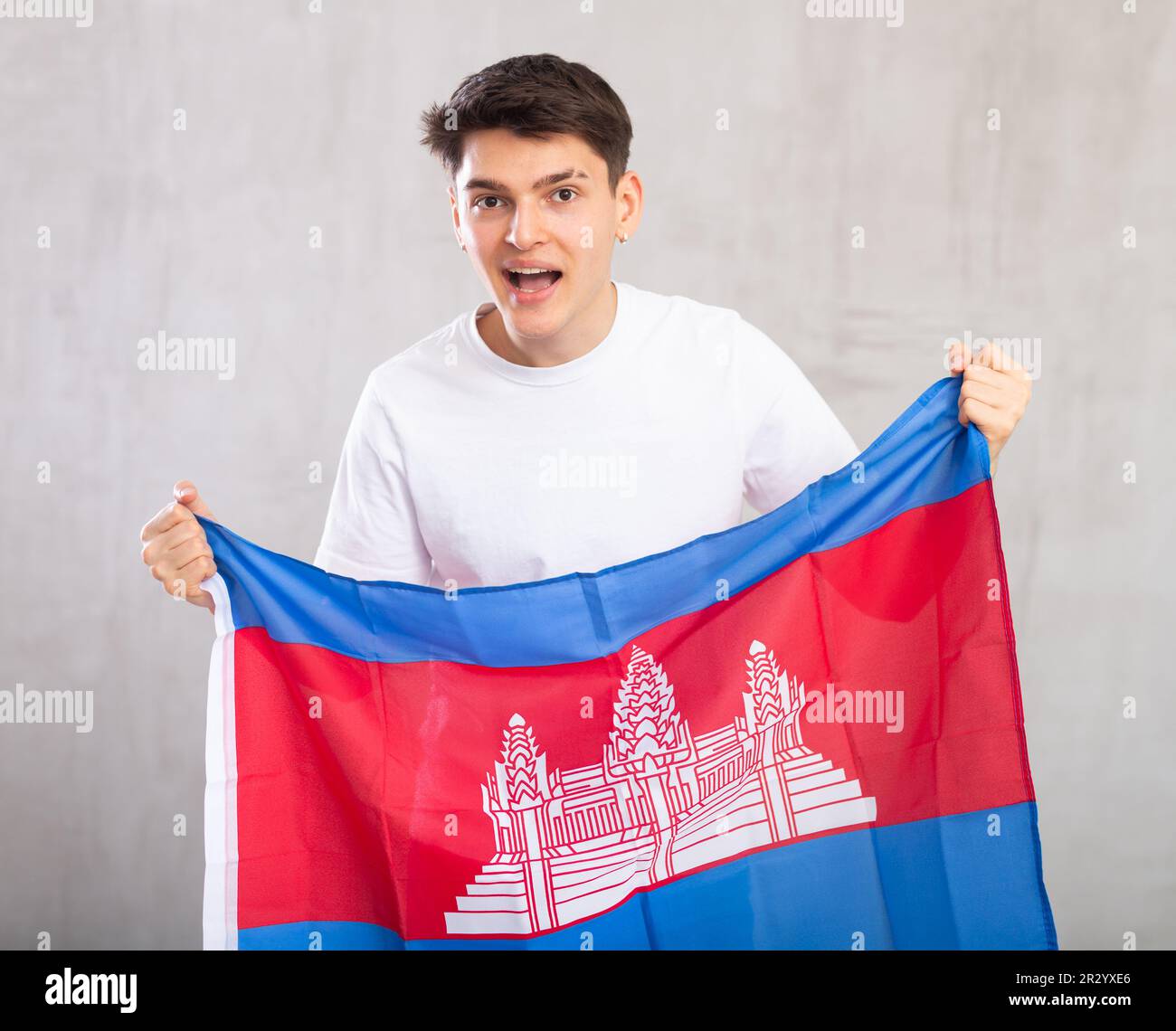 Eccitato, attivo spettatore maschile tiene bandiera nazionale della Cambogia in mani e canti slogan popolare. Foto Stock