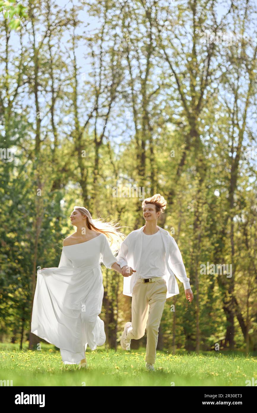 Sposi felici che tengono le mani e corrono sul prato in una giornata di sole Foto Stock