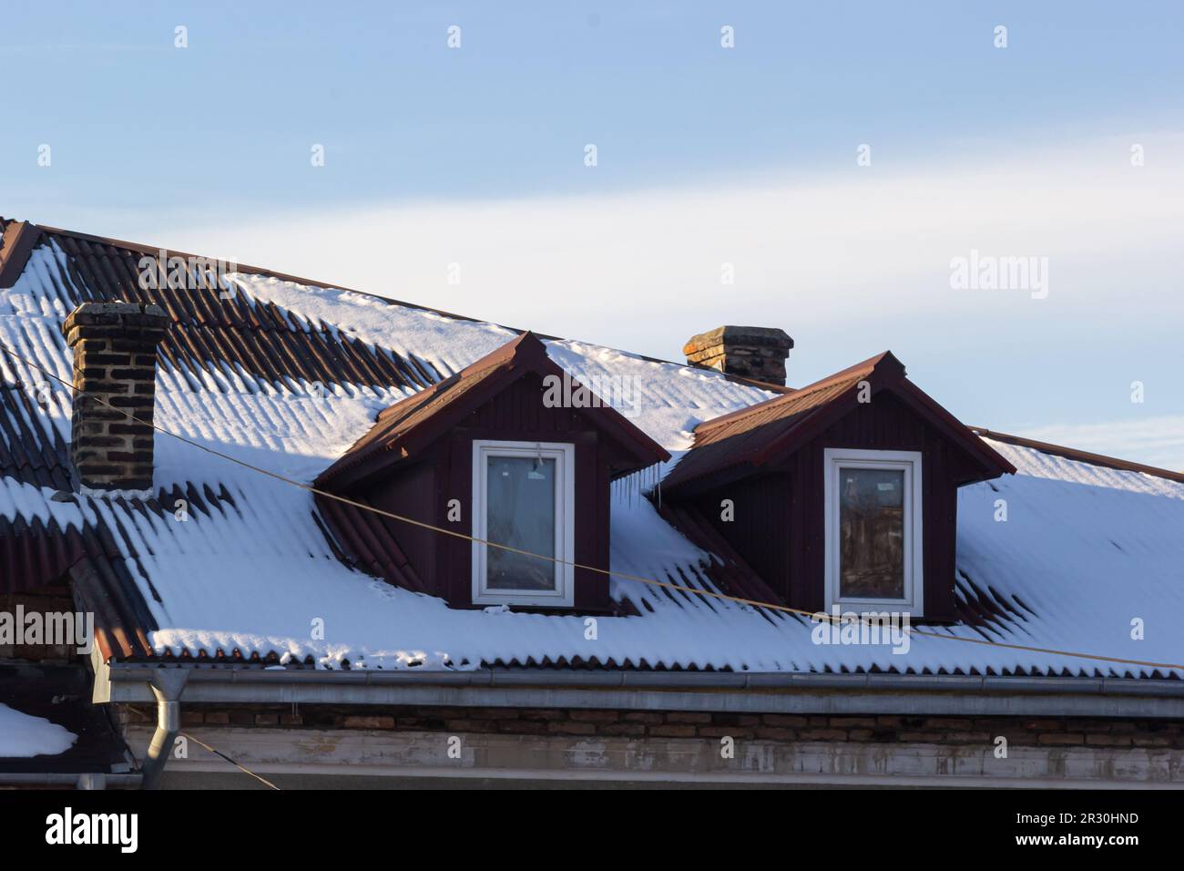 Neve sul tetto di una mattonella di metallo rossa e marrone di una casa europea. Foto Stock