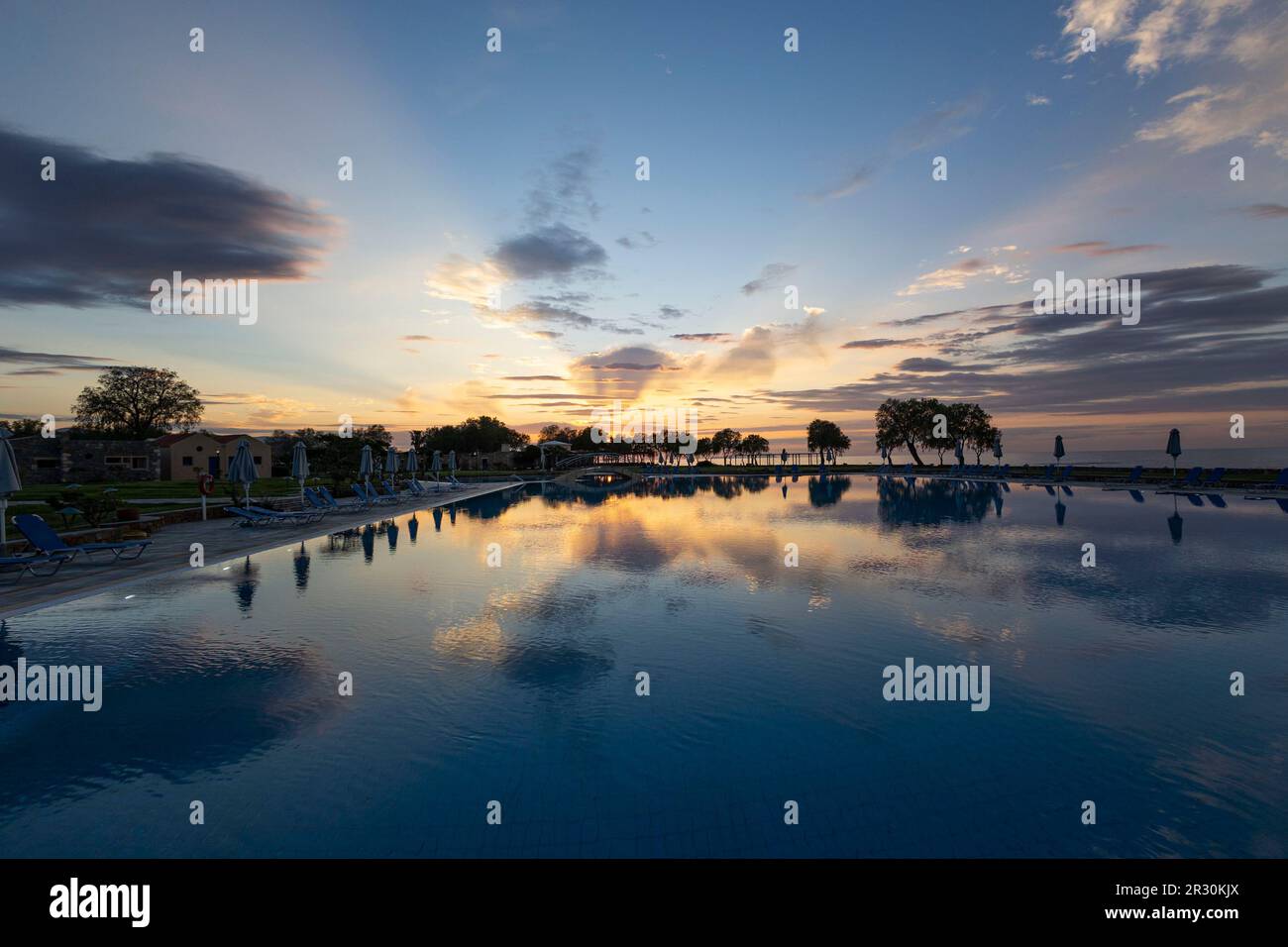 Piscina all'aperto nella località di Kalimera Kriti al tramonto con riflessione in acqua, Sisi, Creta, Grecia, Europa. Foto Stock