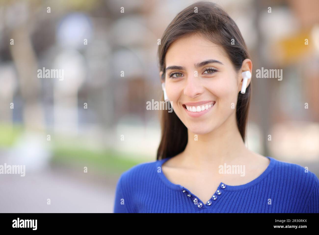 Donna felice con auricolari in piedi e in posa guardando la macchina fotografica in strada Foto Stock