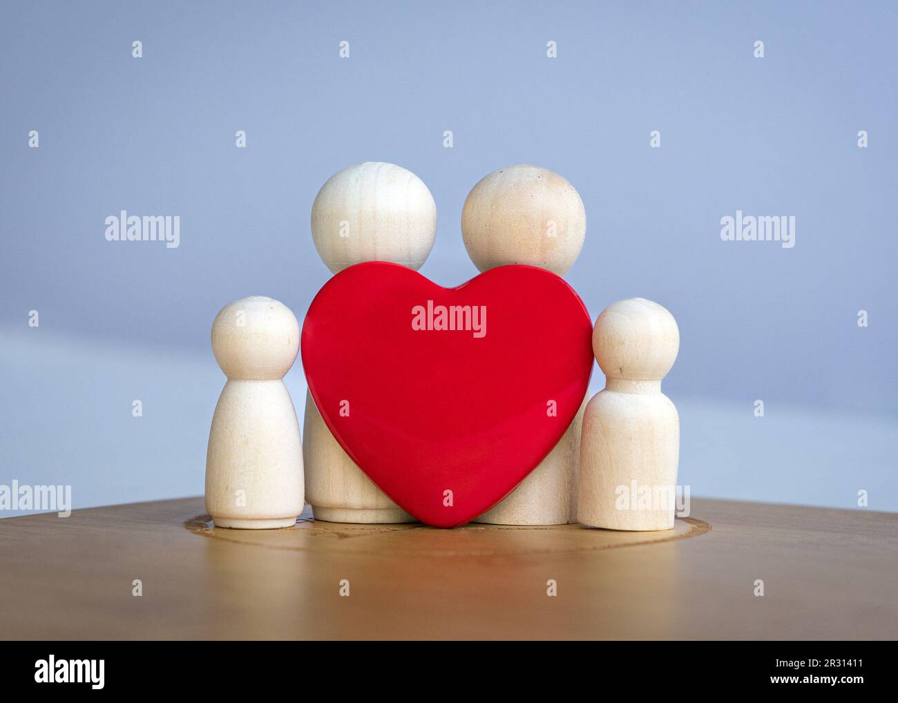 Bambole di legno raffiguranti padre, madre, figlio e figlia a forma di cuore rosso. Concetto di famiglia di amore. Foto Stock
