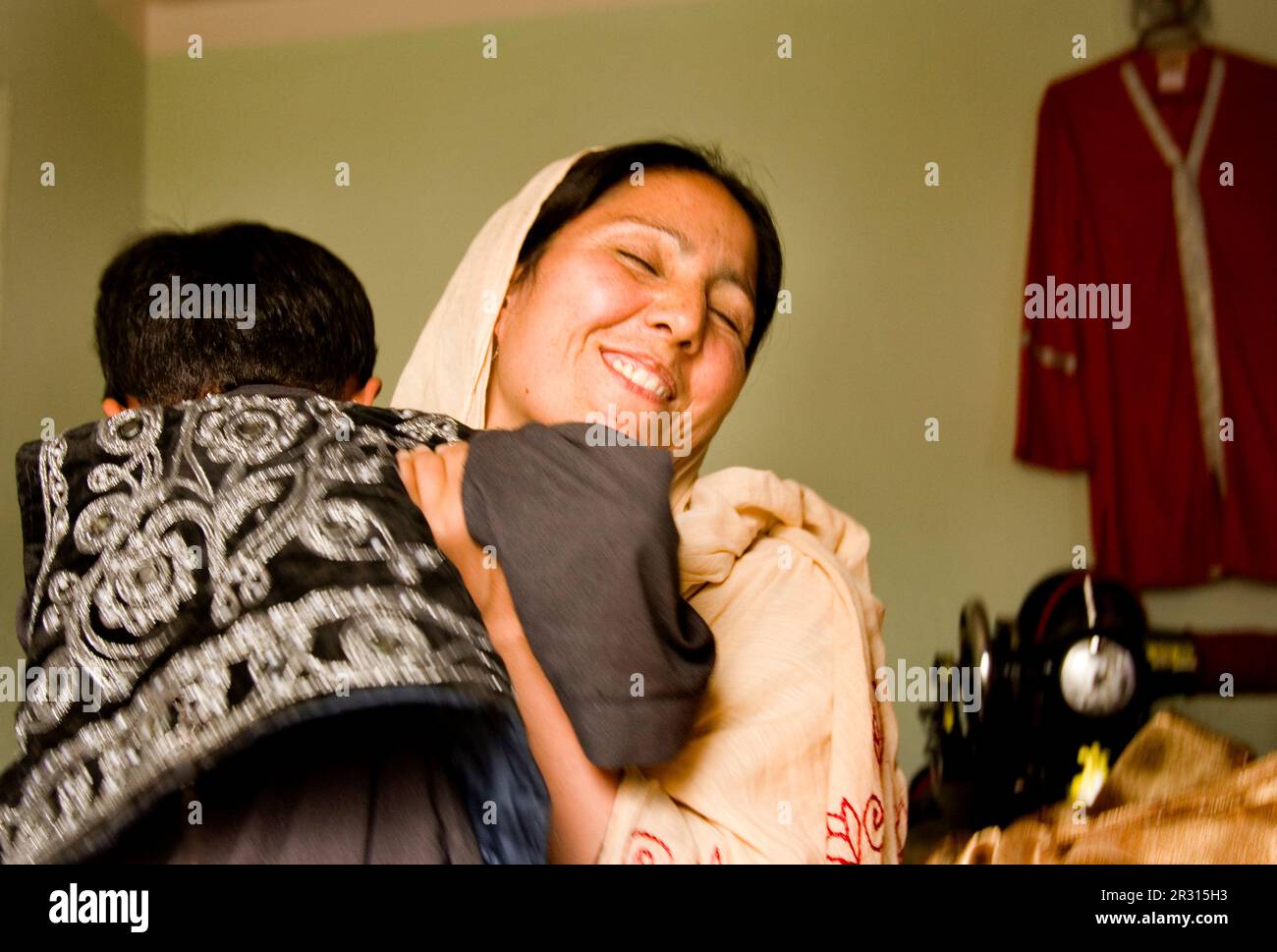 La donna scopa il suo figlio giovane quando freccette nel suo laboratorio di cucito a Kabul. Foto Stock