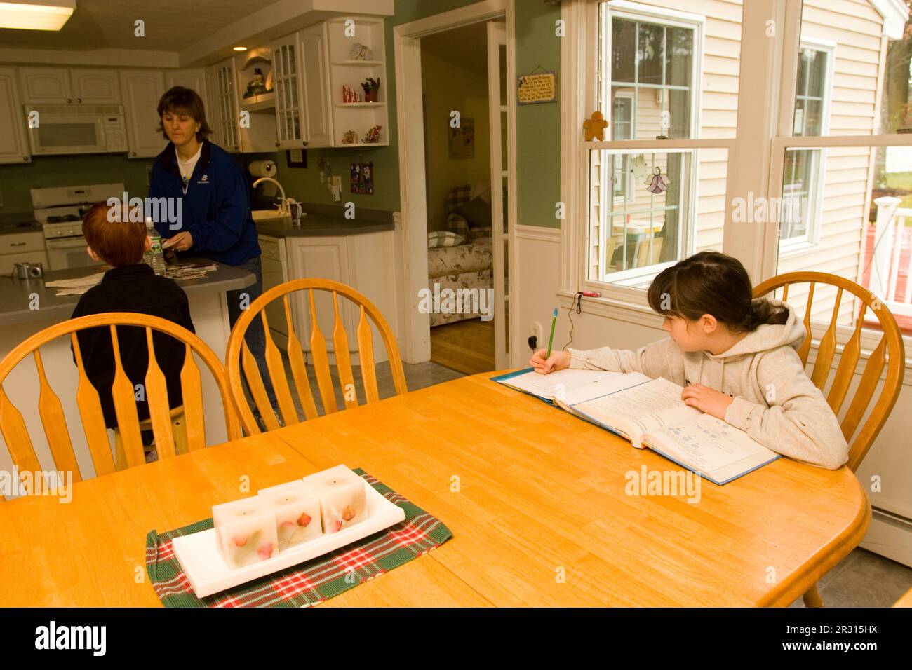 Una ragazza di dieci anni si siede al suo tavolo da cucina facendo i compiti a casa in un pomeriggio di fine settimana. Foto Stock