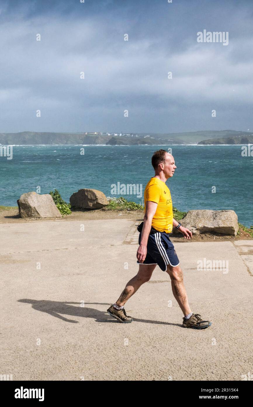 Un uomo che indossa pantaloncini a piedi lungo la strada costiera a Towan Head che si affaccia sulla Newquay Bay in Cornovaglia nel Regno Unito. Foto Stock