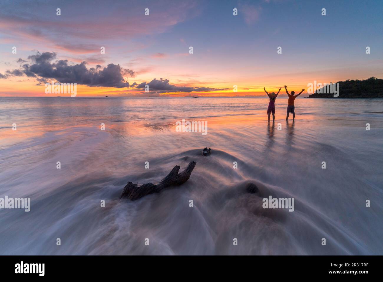 Allegro uomo e donna con le braccia alzate al tramonto, Mar dei Caraibi Foto Stock