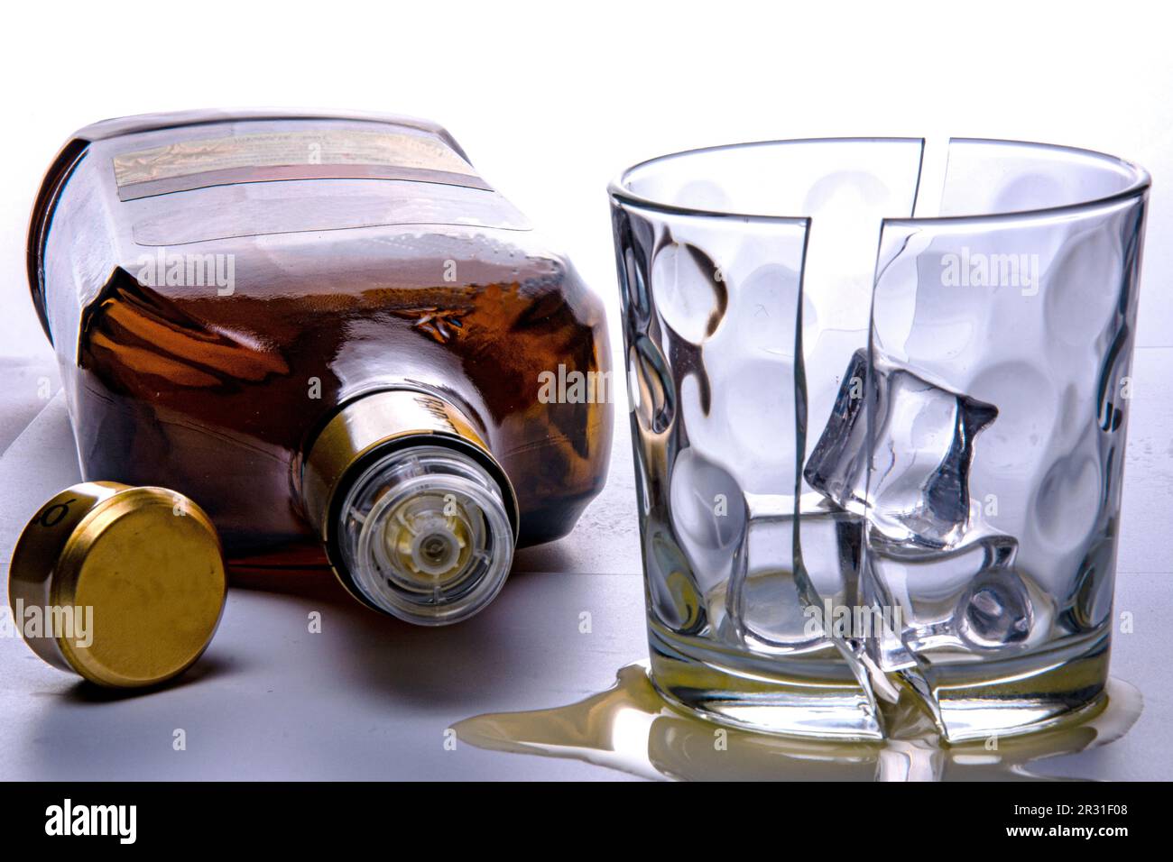 Bottiglia di rum vuota e bicchiere rotto in due metà con tre cubetti di ghiaccio. Fotografato su sfondo bianco nello studio. Ancora la vita al buio. Foto Stock