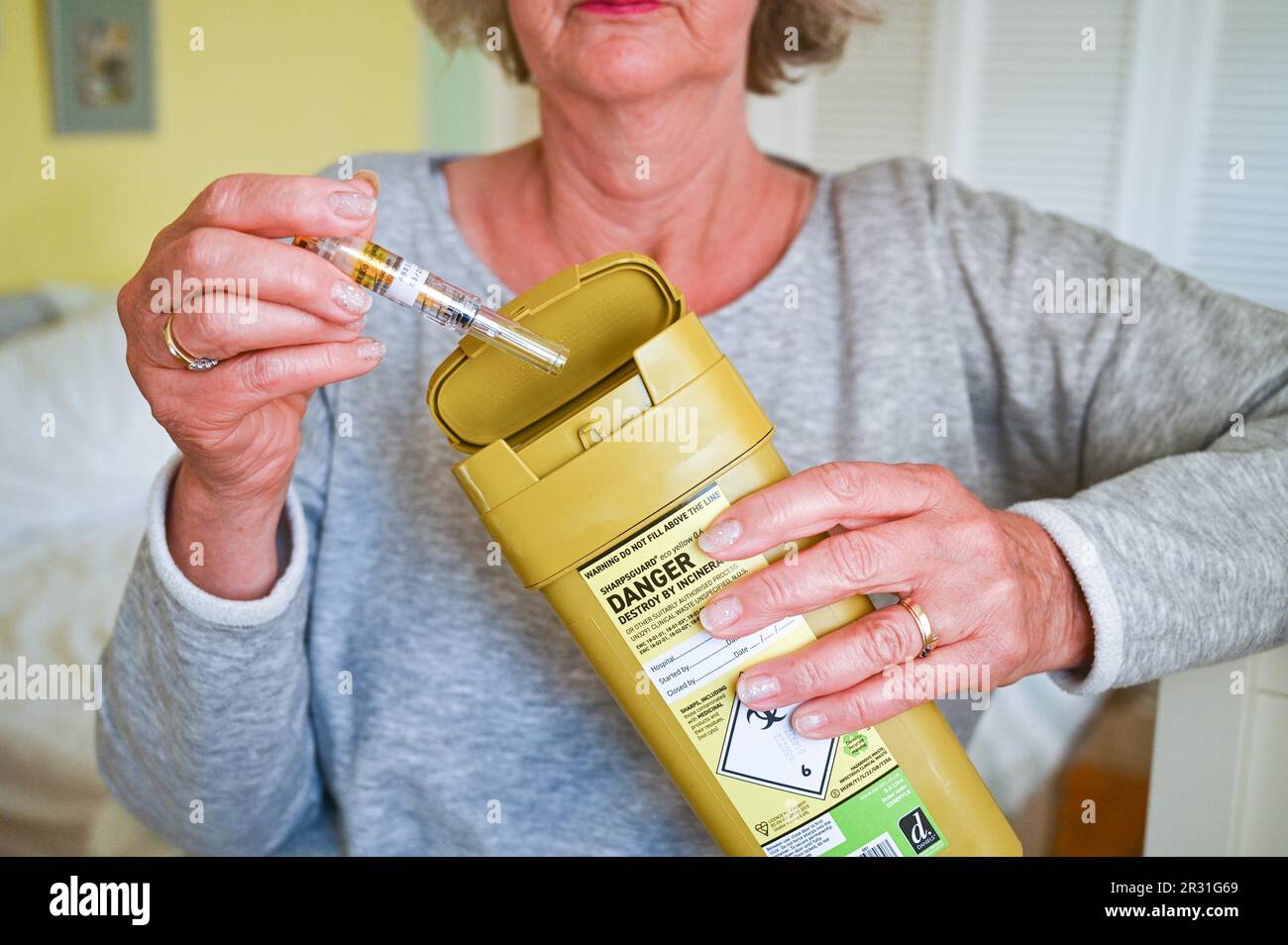 Donna che smaltisce un ago usato in un'unità di smaltimento Sharpsguard o in un contenitore per oggetti taglienti Foto Stock