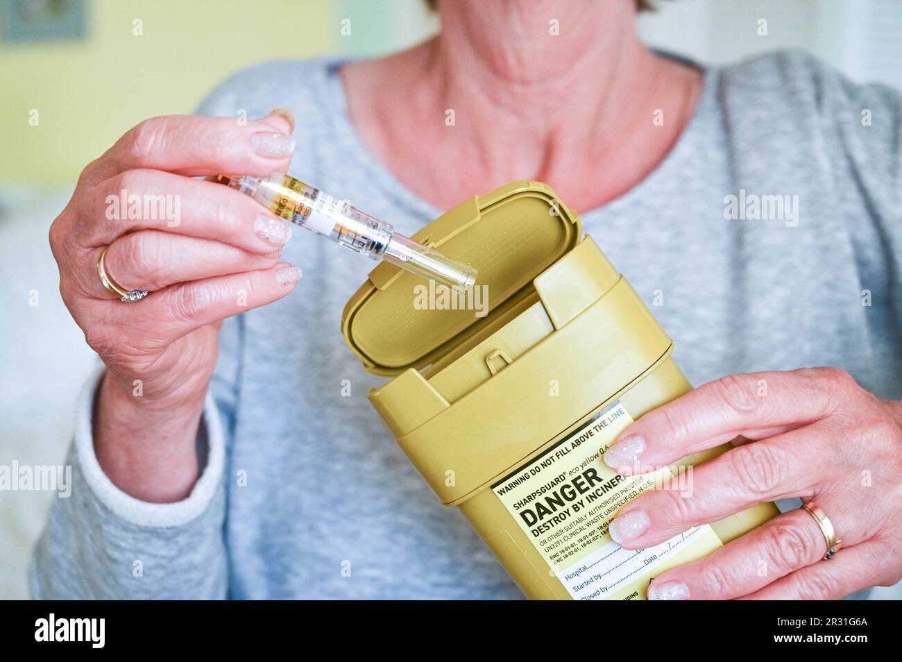 Donna che smaltisce un ago usato in un'unità di smaltimento Sharpsguard o in un contenitore per oggetti taglienti Foto Stock