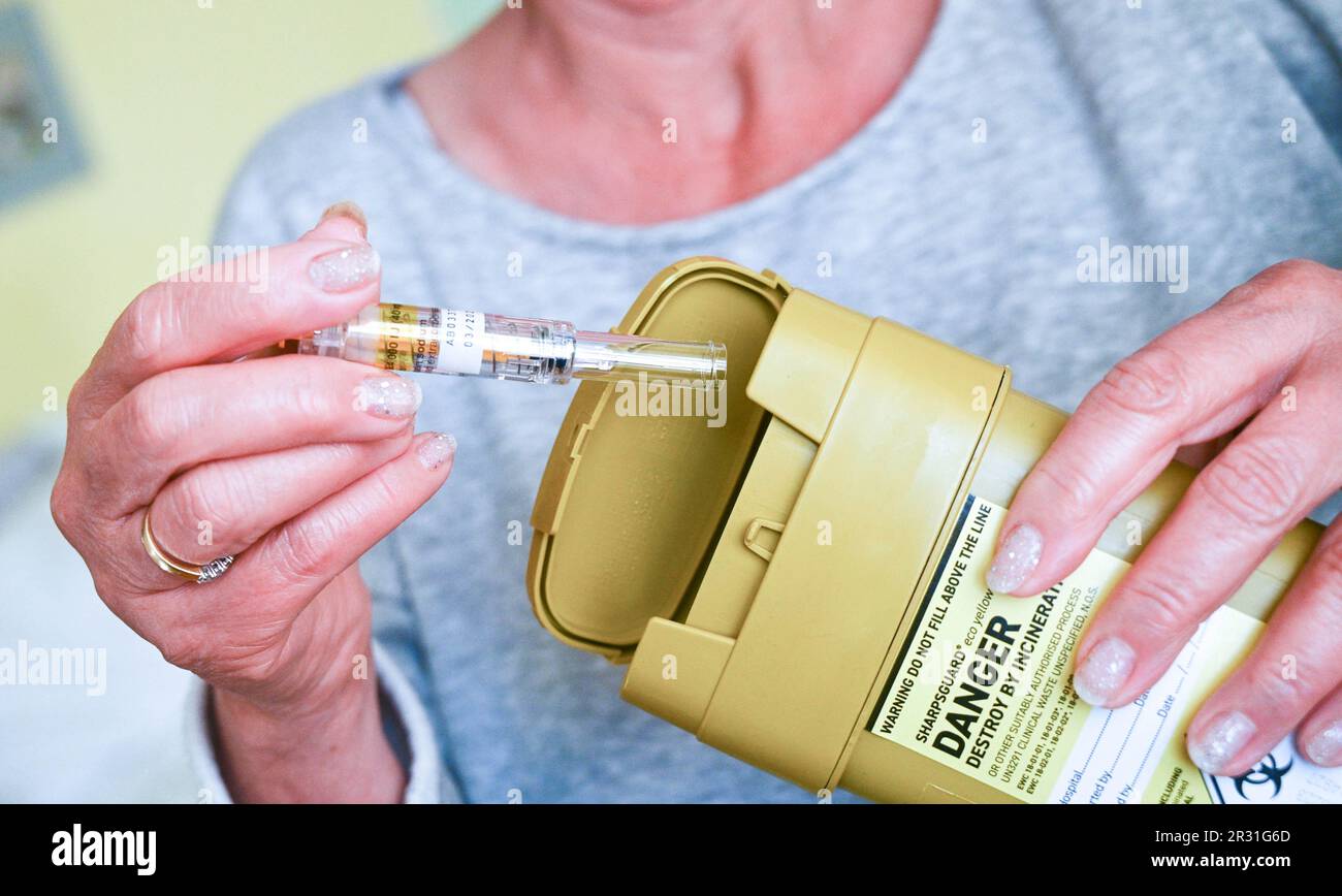 Donna che smaltisce un ago usato in un'unità di smaltimento Sharpsguard o in un contenitore per oggetti taglienti Foto Stock