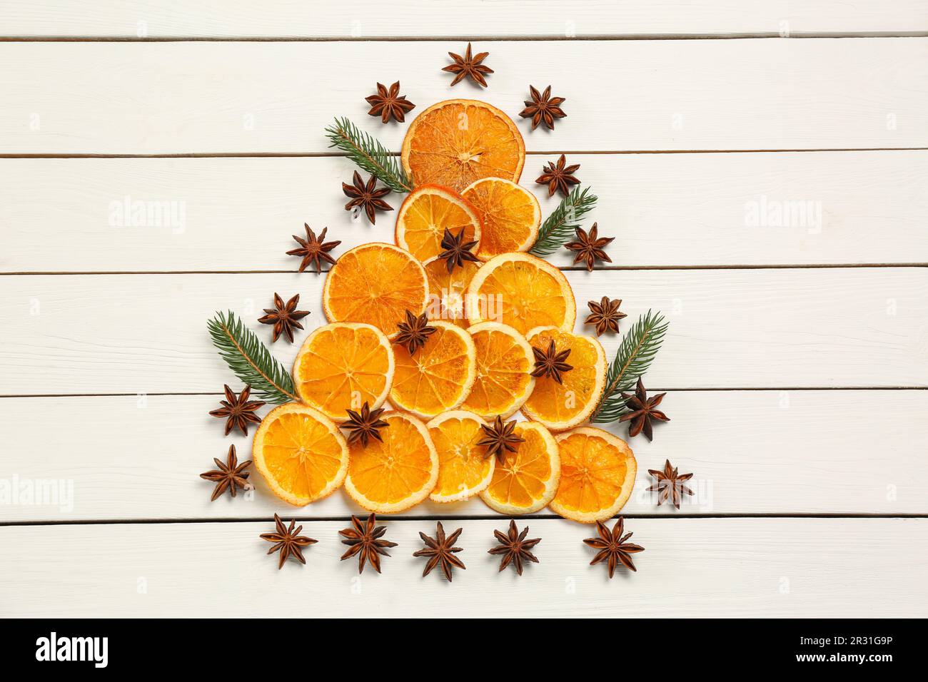 Composizione di posa piatta con fettine di arancio secco, rami di abete e stelle di anice disposte a forma di albero di Natale su tavola di legno bianco Foto Stock